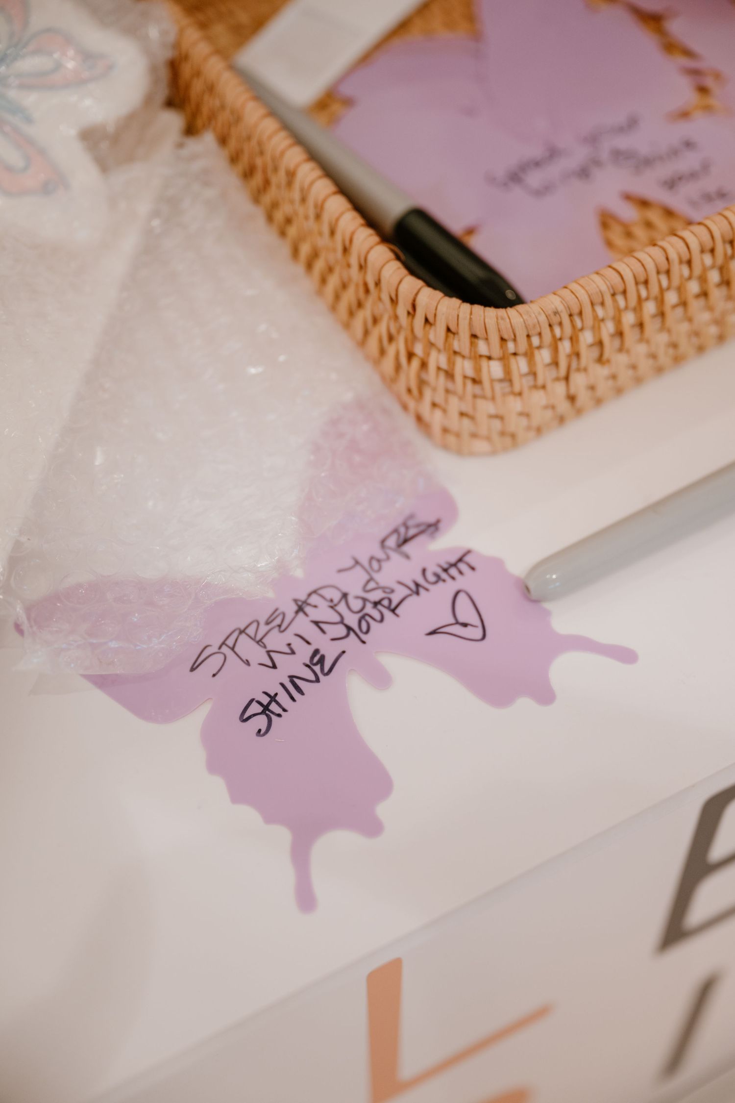 Purple butterfly cutout with handwritten inspirational message on white surface near wicker basket.