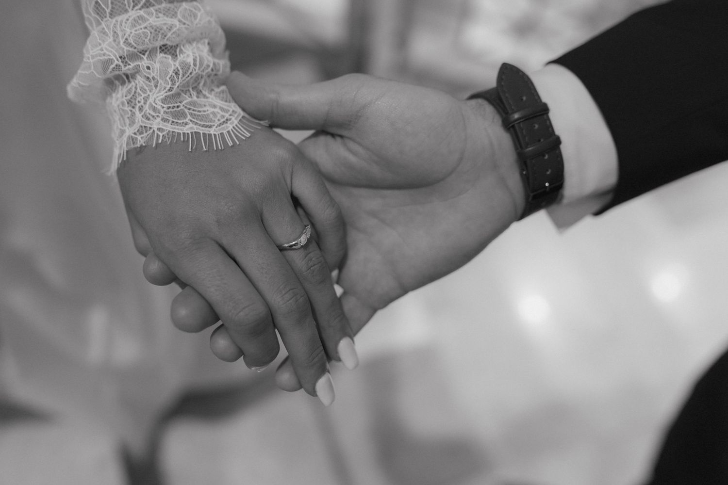 Black and white close-up of bride and groom holding hands showing wedding rings.