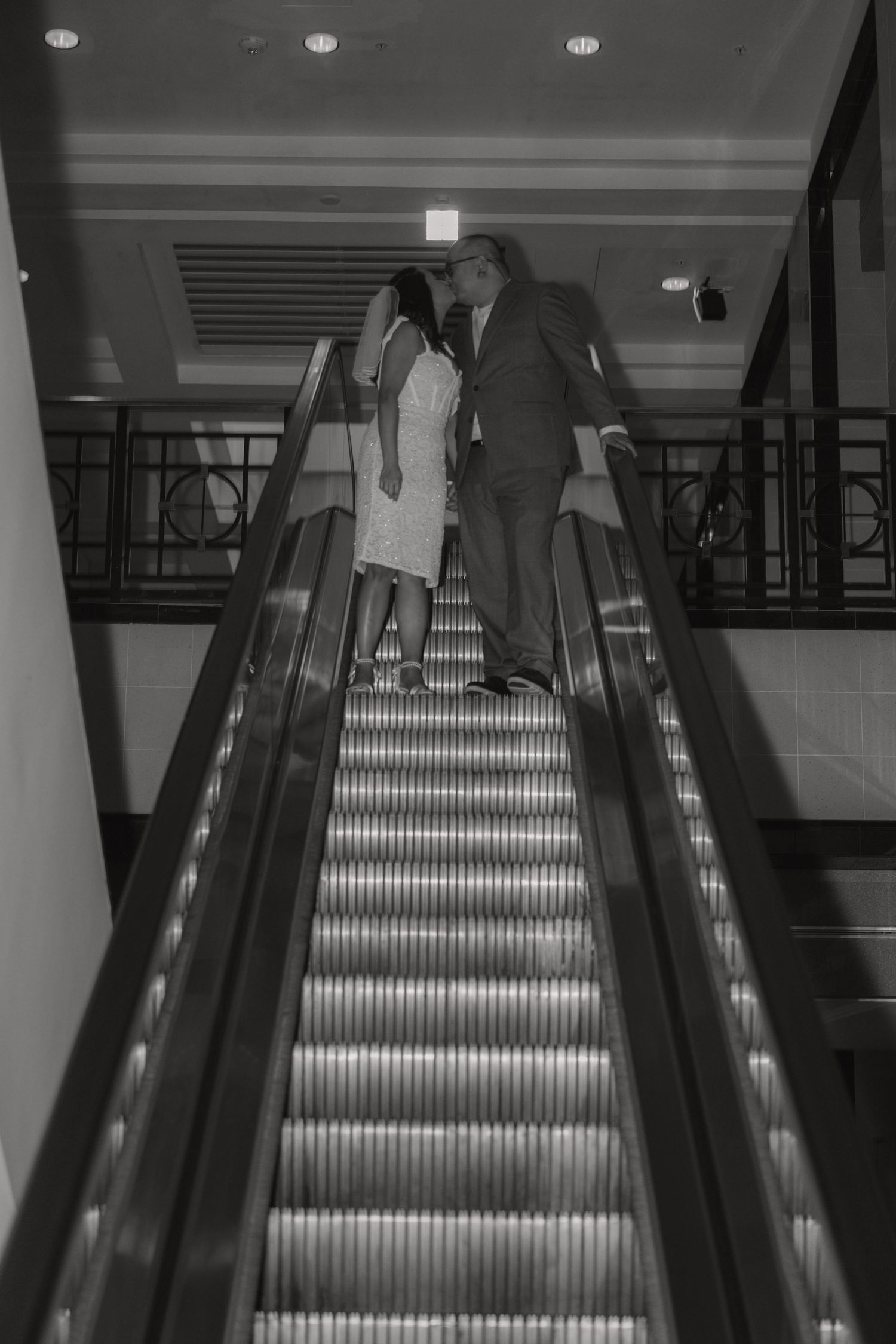 Newlywed couple sharing a romantic kiss on an escalator after their wedding ceremony.