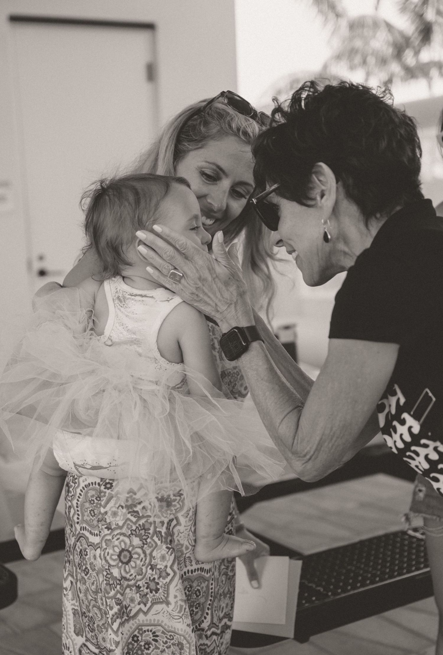 Black and white photo of a mother holding her baby while an older woman lovingly touches the child's face.