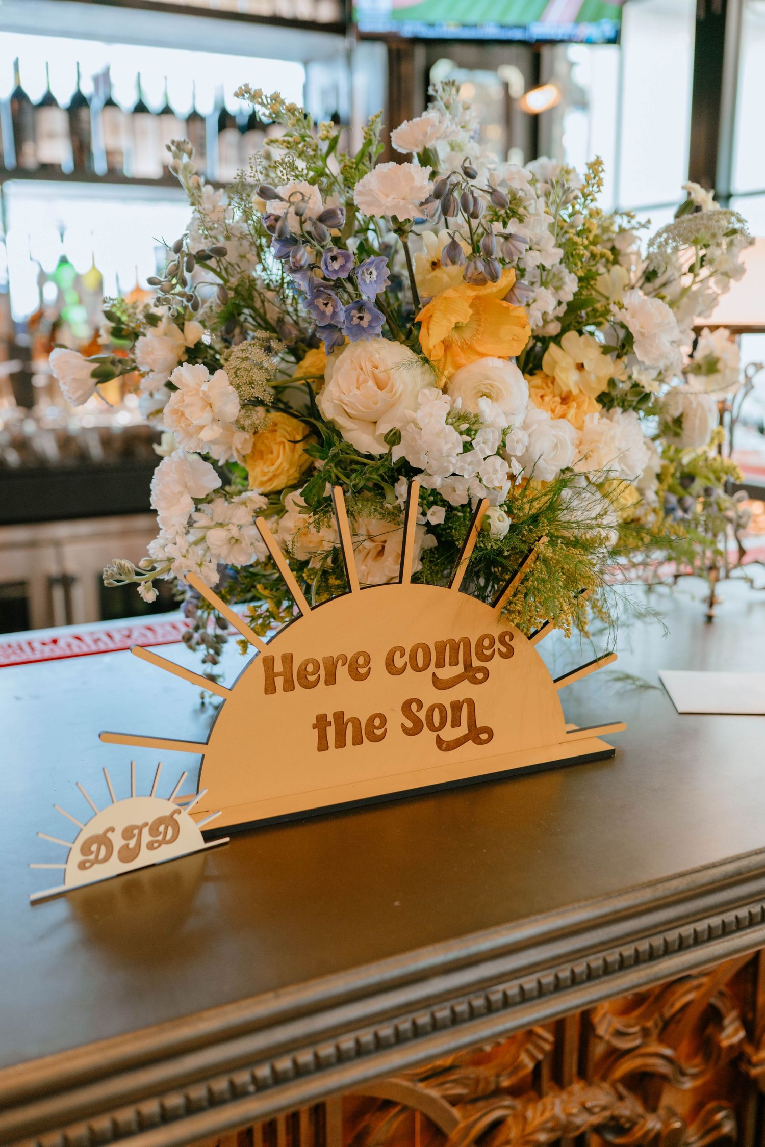 Here Comes the Son baby shower wooden sign surrounded by yellow and white floral arrangement on ornate table.
