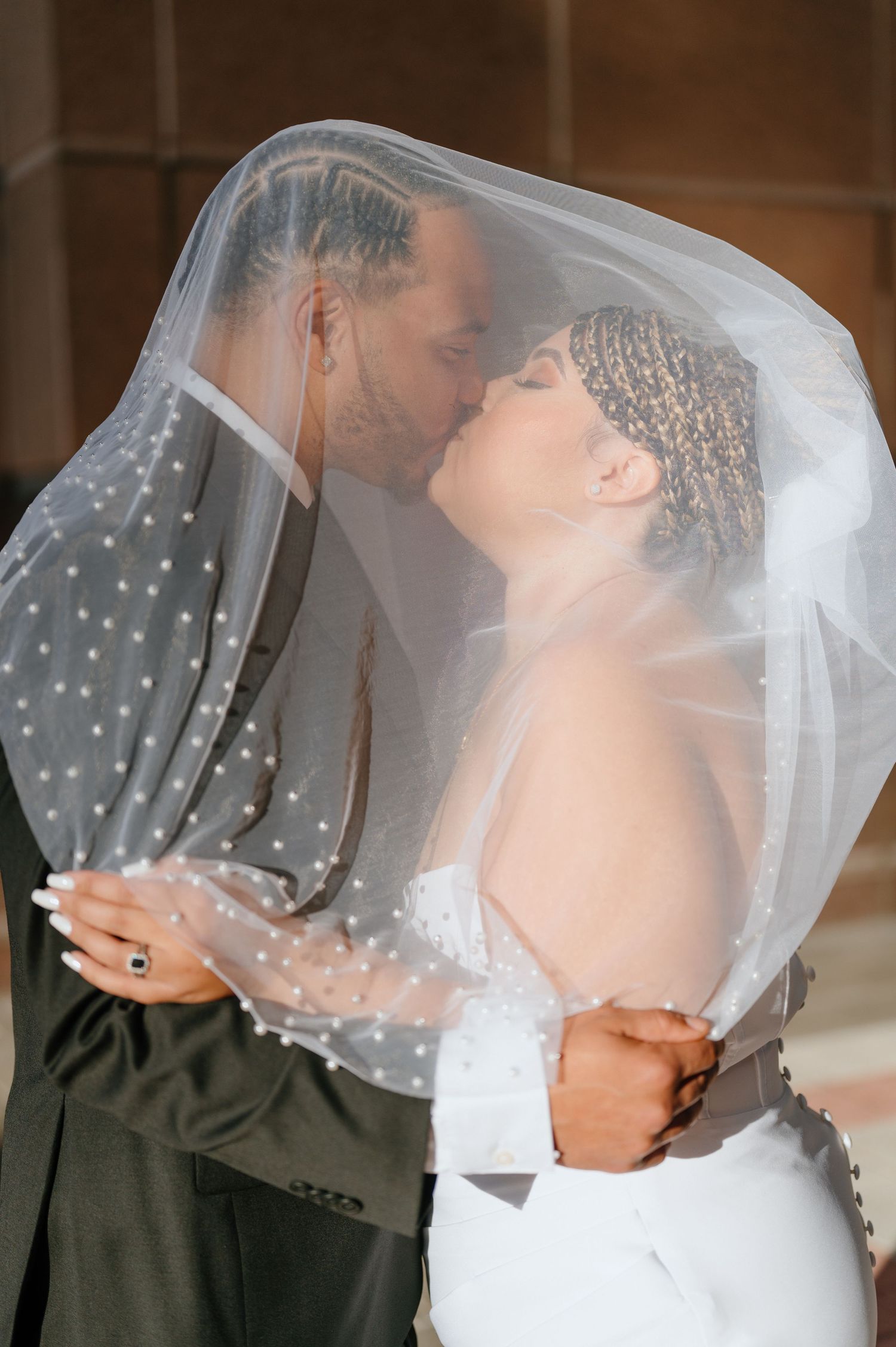 Bride and groom sharing a passionate kiss under a polka dot wedding veil in an archway.