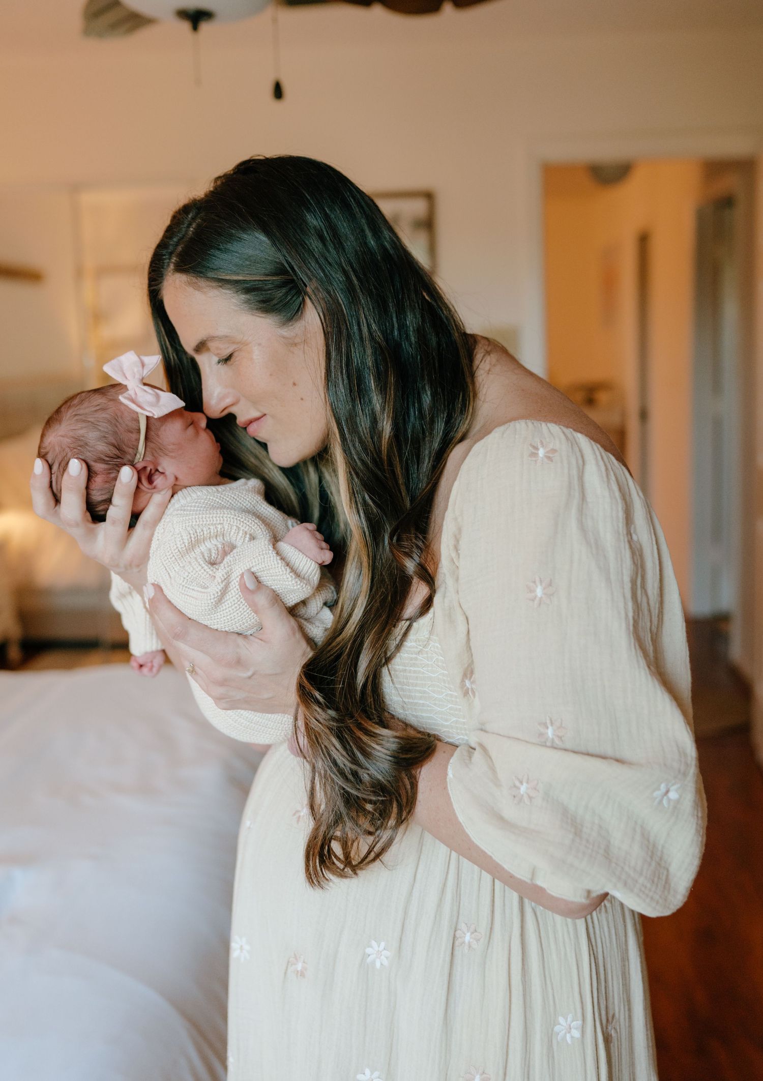 Mother in white floral dress tenderly kissing her newborn baby girl.