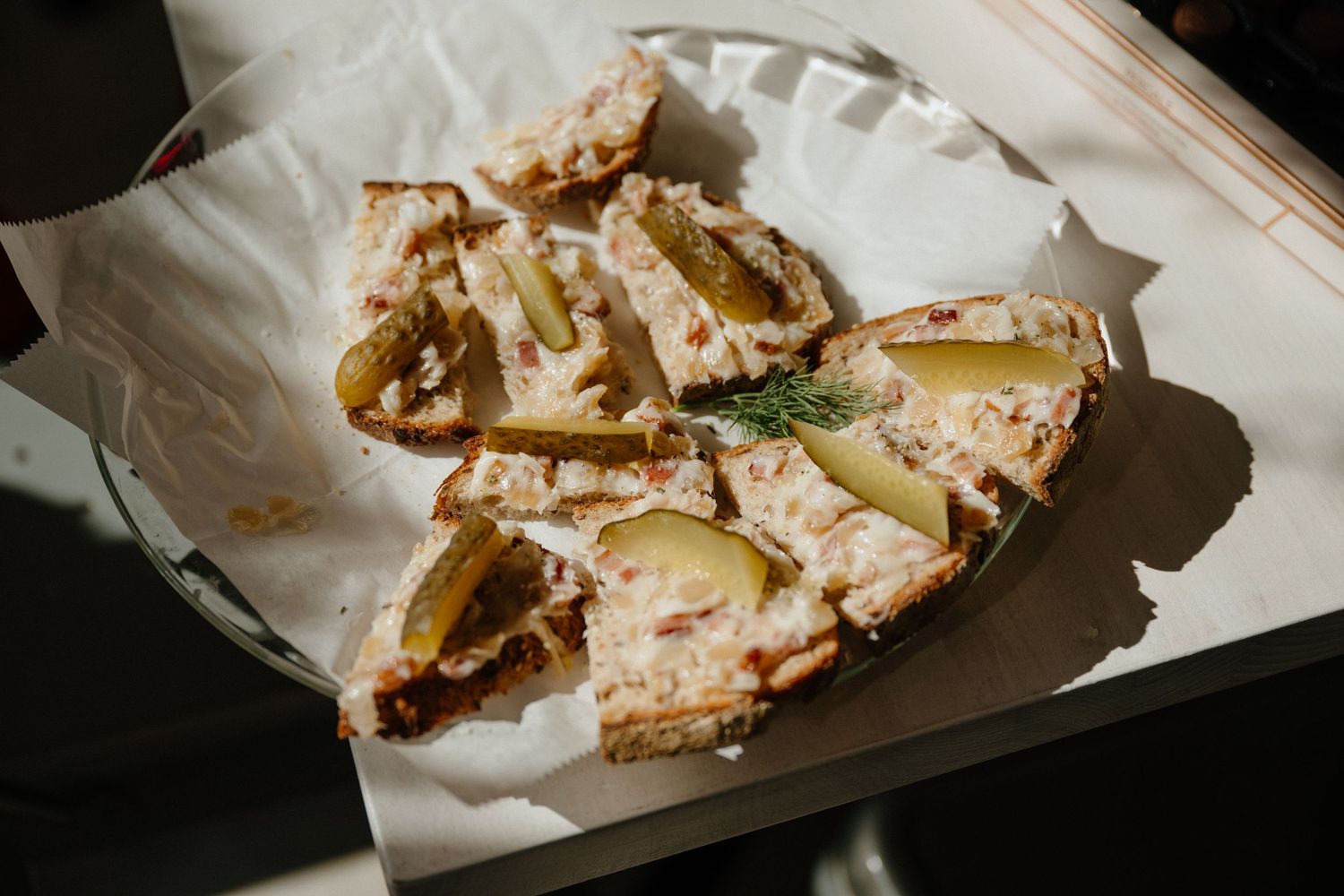 Open-faced Polish sandwich with creamy spread, pickles, and dill herb garnish served on white paper.