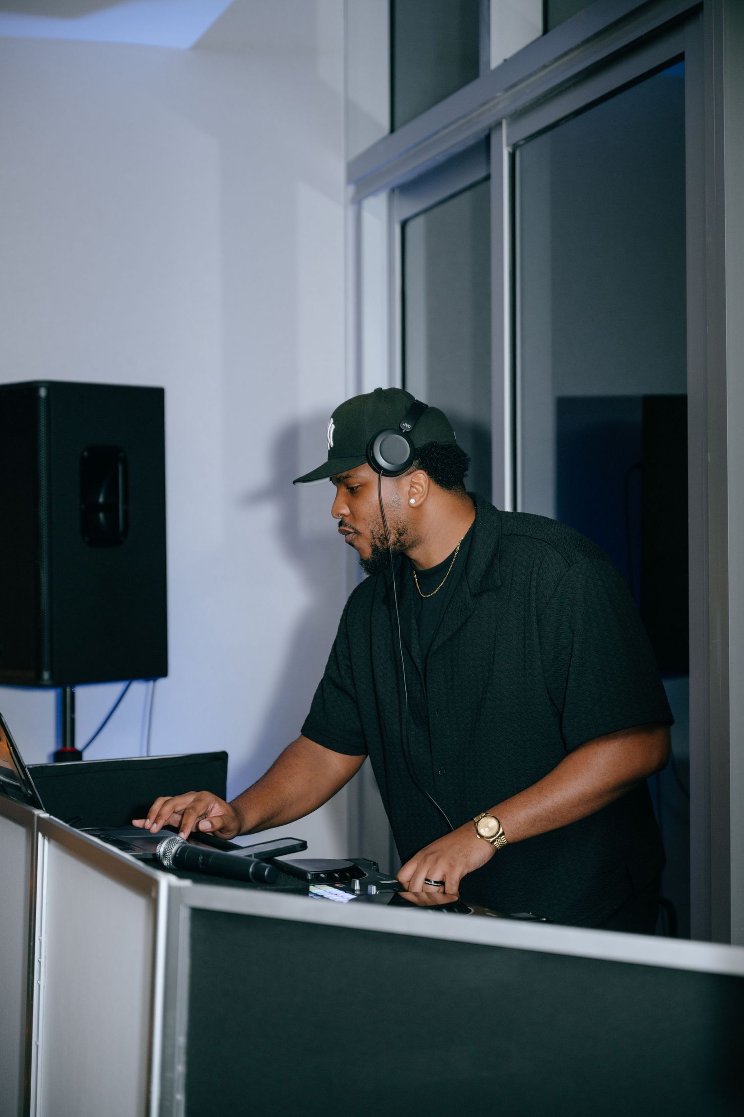 DJ in black outfit and cap mixing music at turntables during a nighttime event.