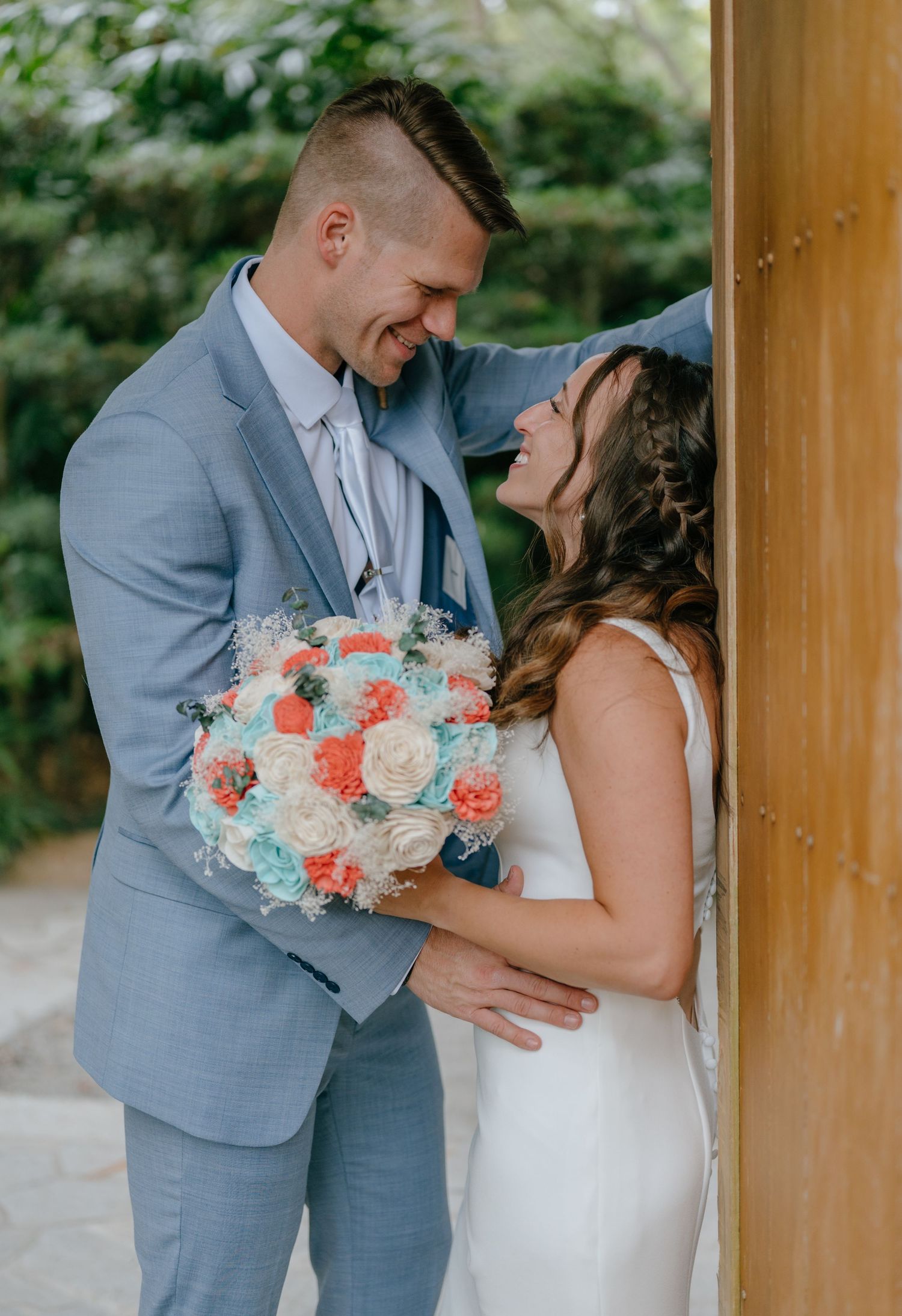Groom and bride share a tender forehead-to-forehead moment holding a coral and teal bouquet.