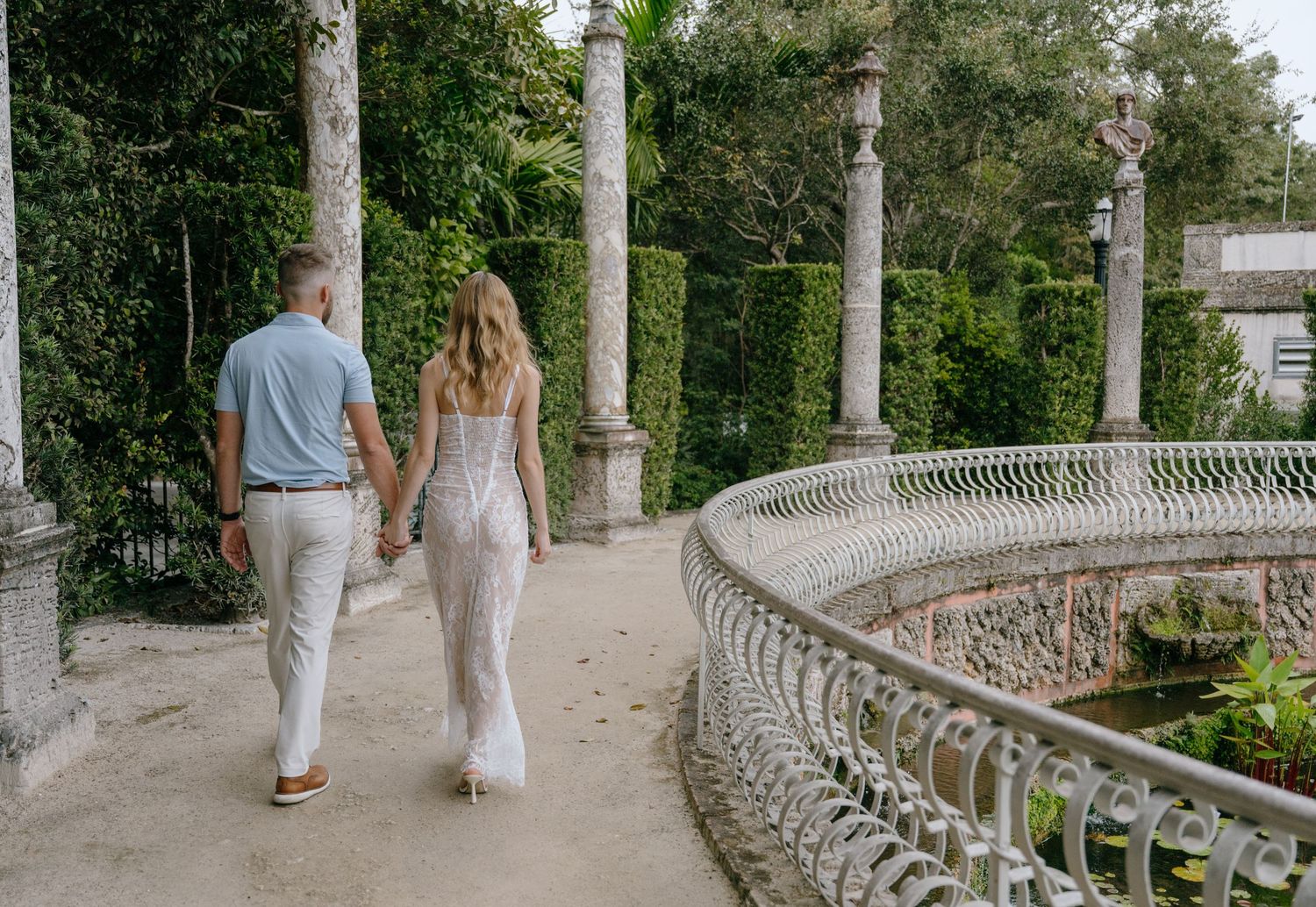 Couple walking hand in hand along a stone path surrounded by lush greenery.