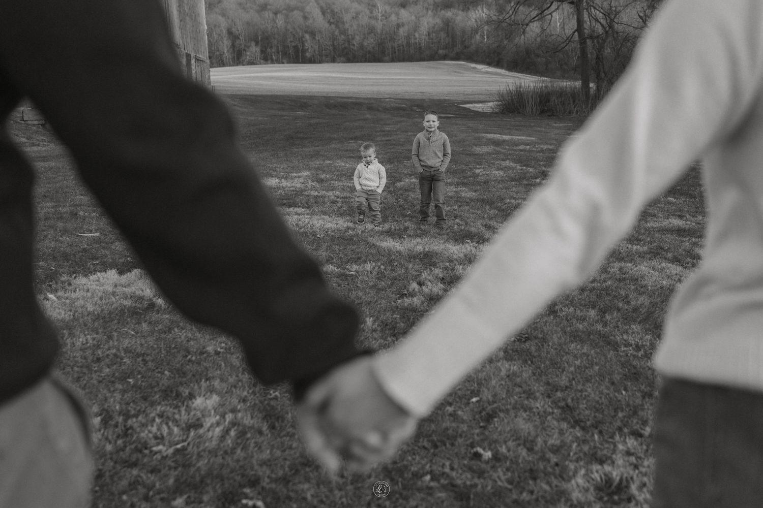 Black and white photo of parents holding hands while two children stand in the background in a field.