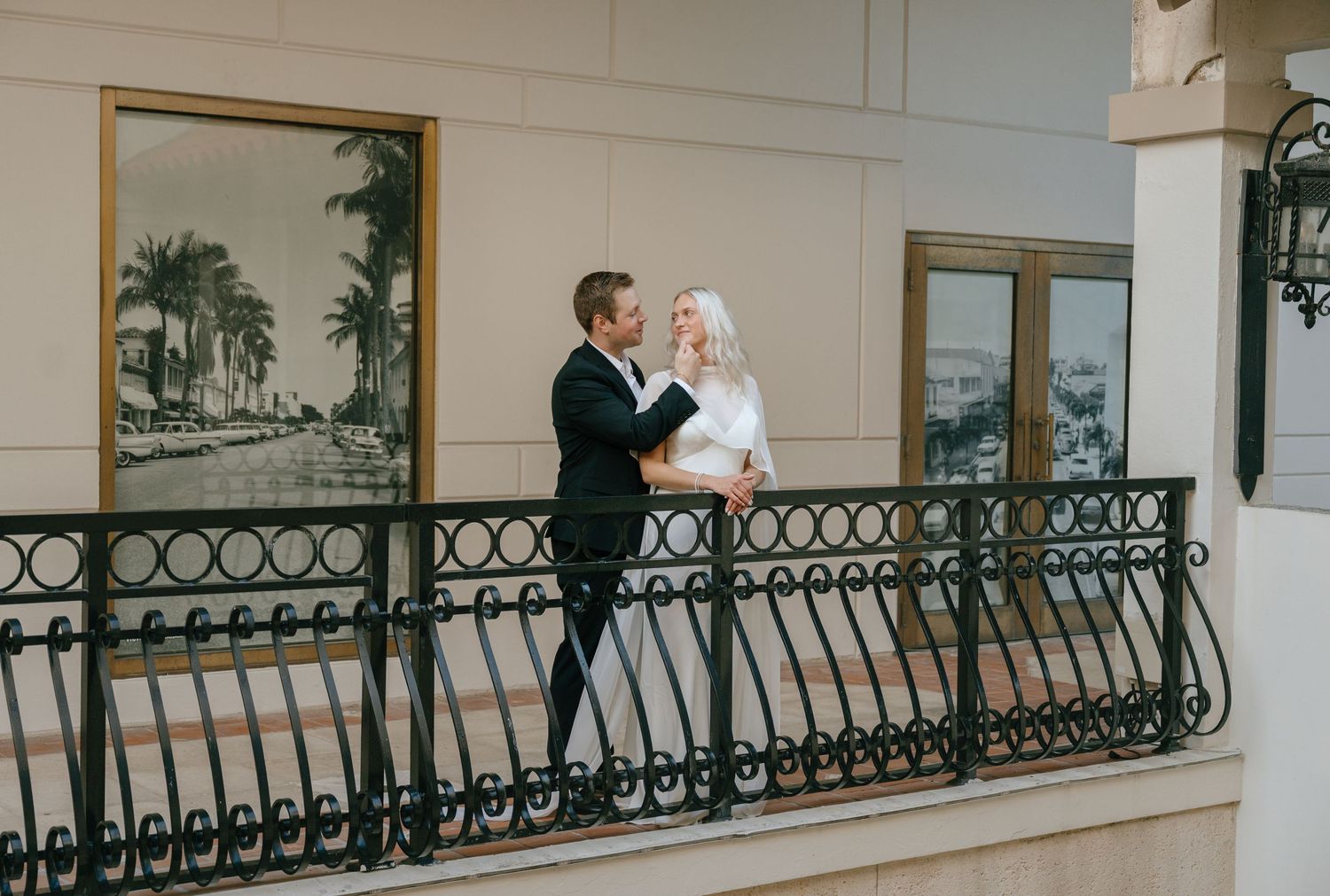 Elegant bride and groom share a tender moment on an ornate iron balcony railing.