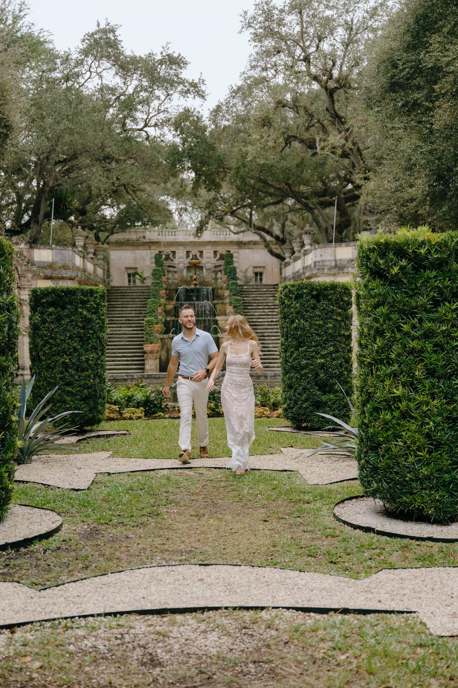 Happy couple walking hand in hand through a manicured garden with hedges.