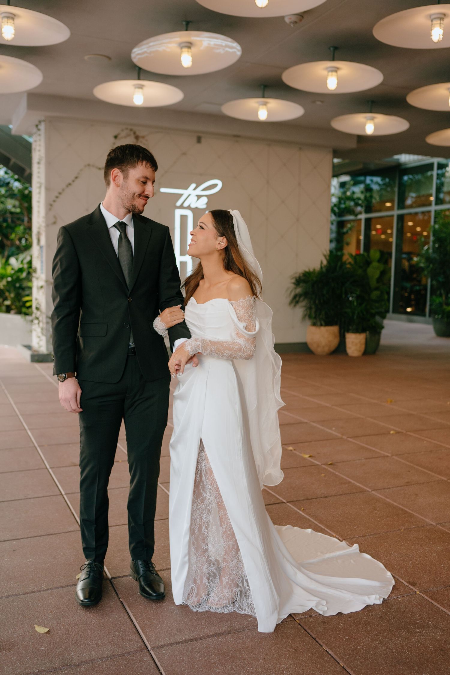 Bride in off-shoulder white gown and groom in black suit at elegant venue.