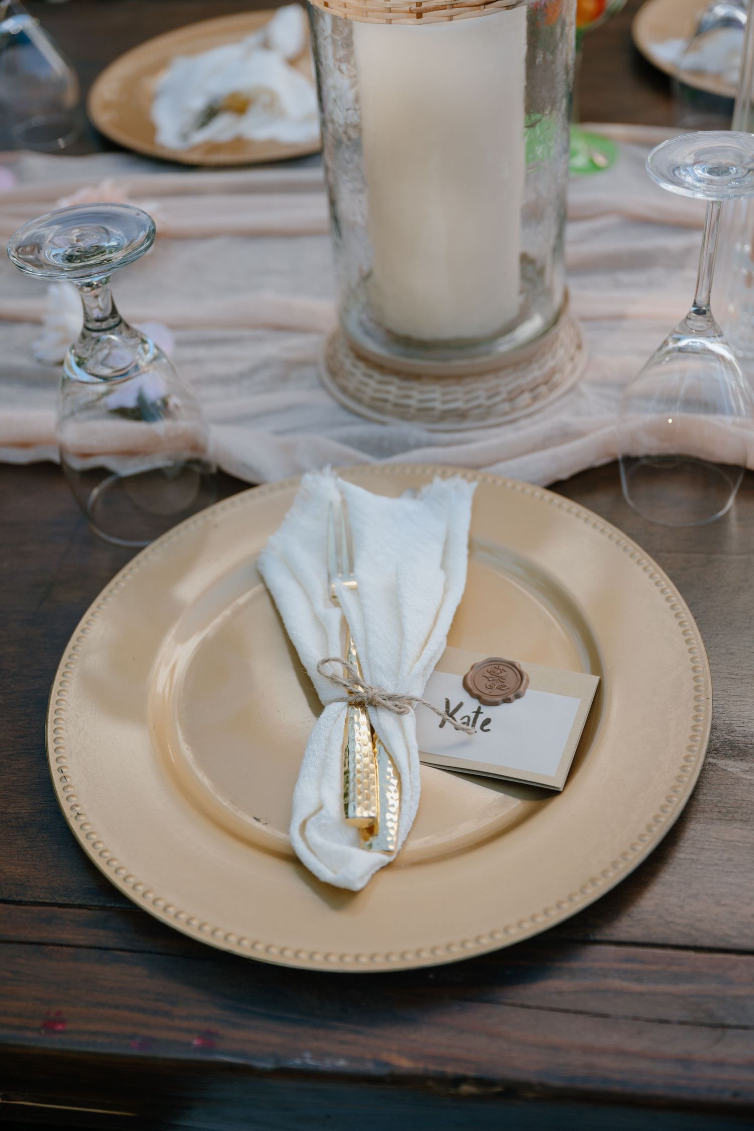 Elegant gold charger plate with white napkin, place card, and candle centerpiece at wedding reception.