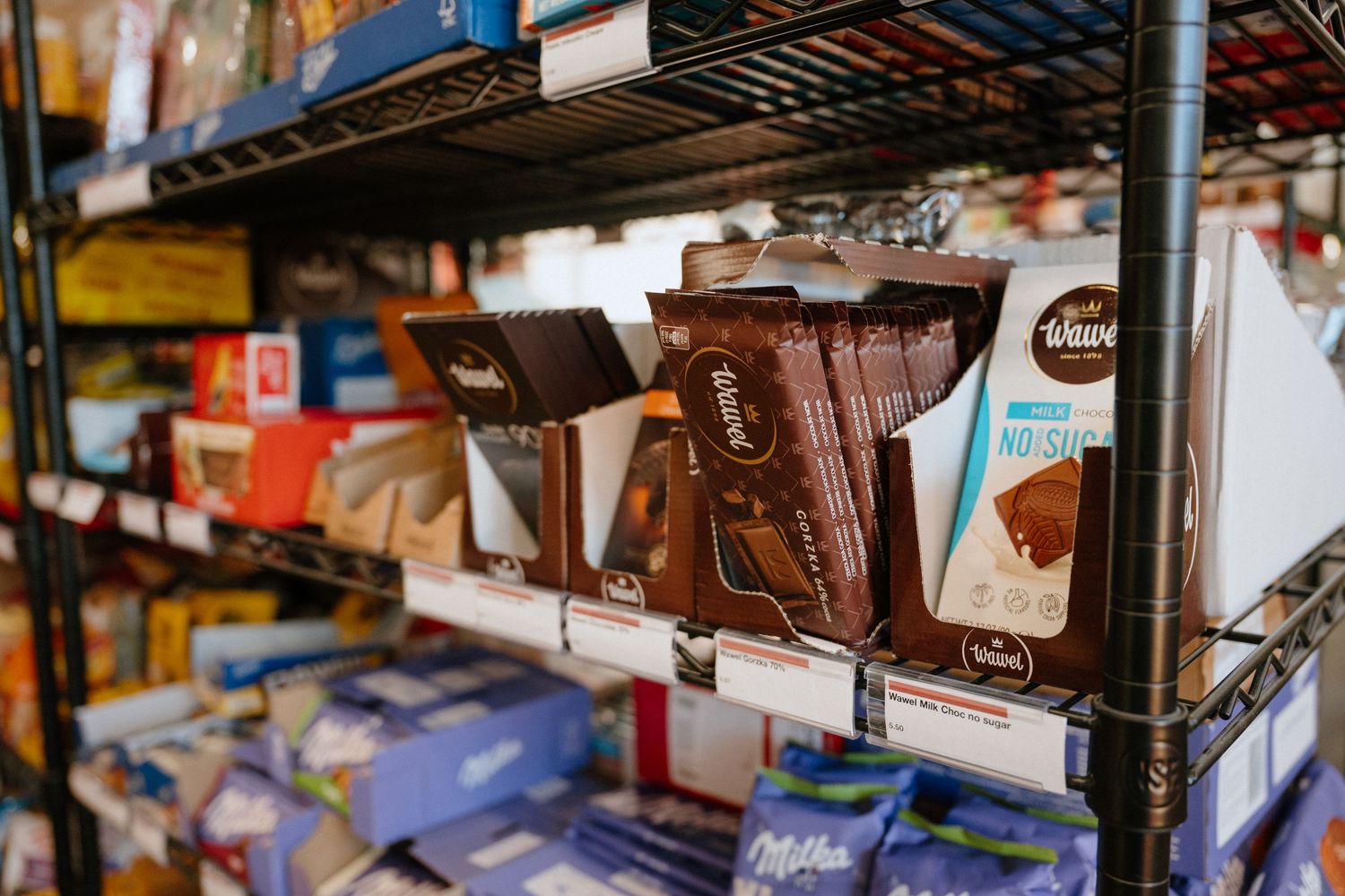 Wawel and Milka chocolate bars displayed on metal shelving in a specialty grocery store.