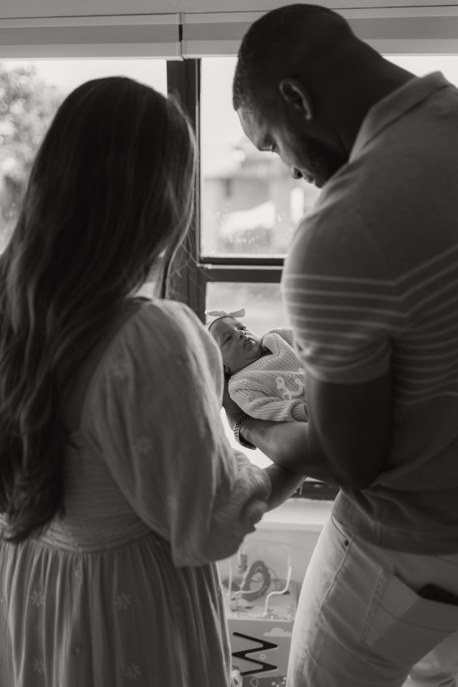 Black and white photo of parents holding their newborn baby by a window.
