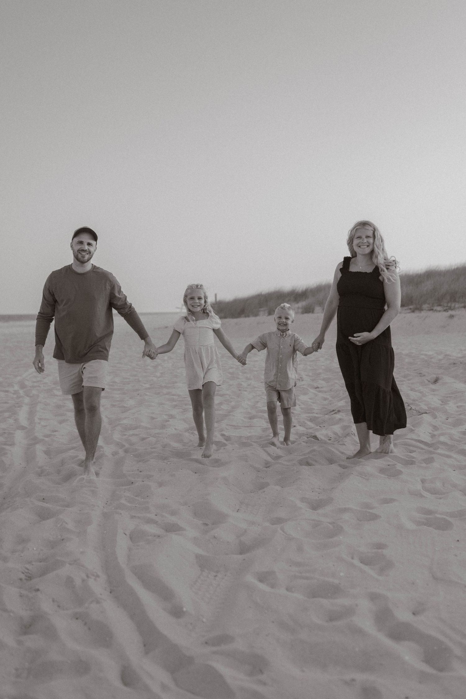 A black and white photo of a pregnant mother and father walking on a beach with two children.