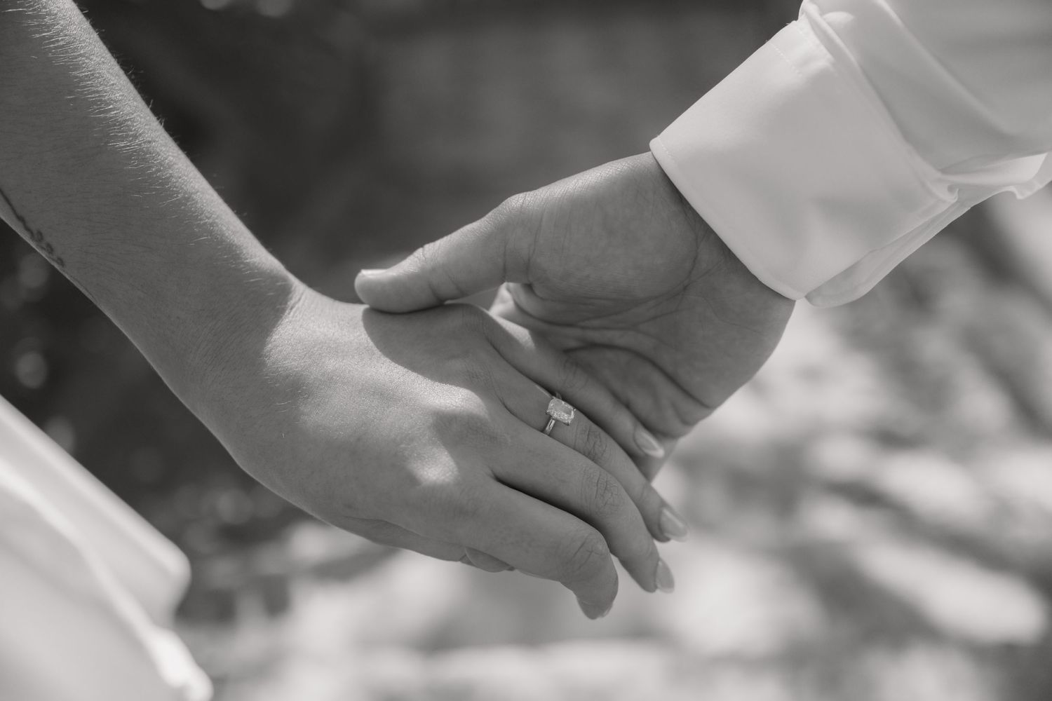 Close-up black and white photo of couple holding hands showing diamond engagement ring.