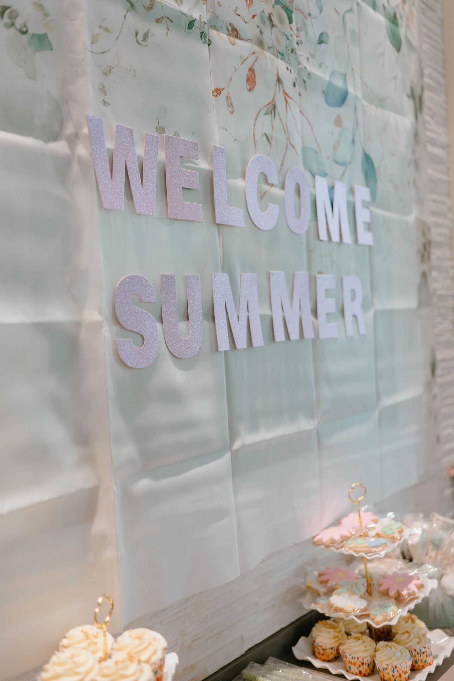 Welcome Summer baby shower backdrop with glittery letters above dessert table with cupcakes.