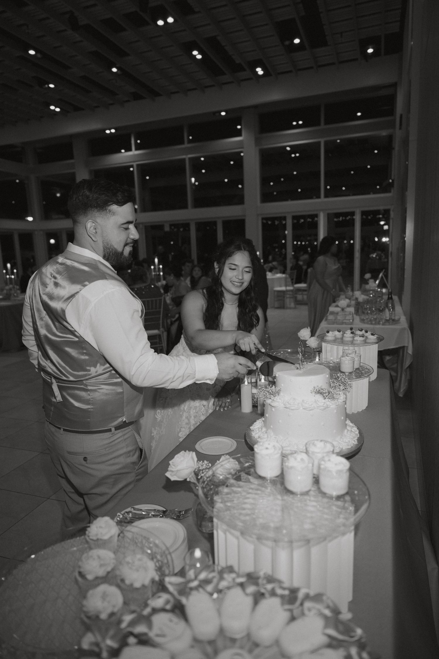 Black and white photo of bride and groom cutting their wedding cake at evening reception.