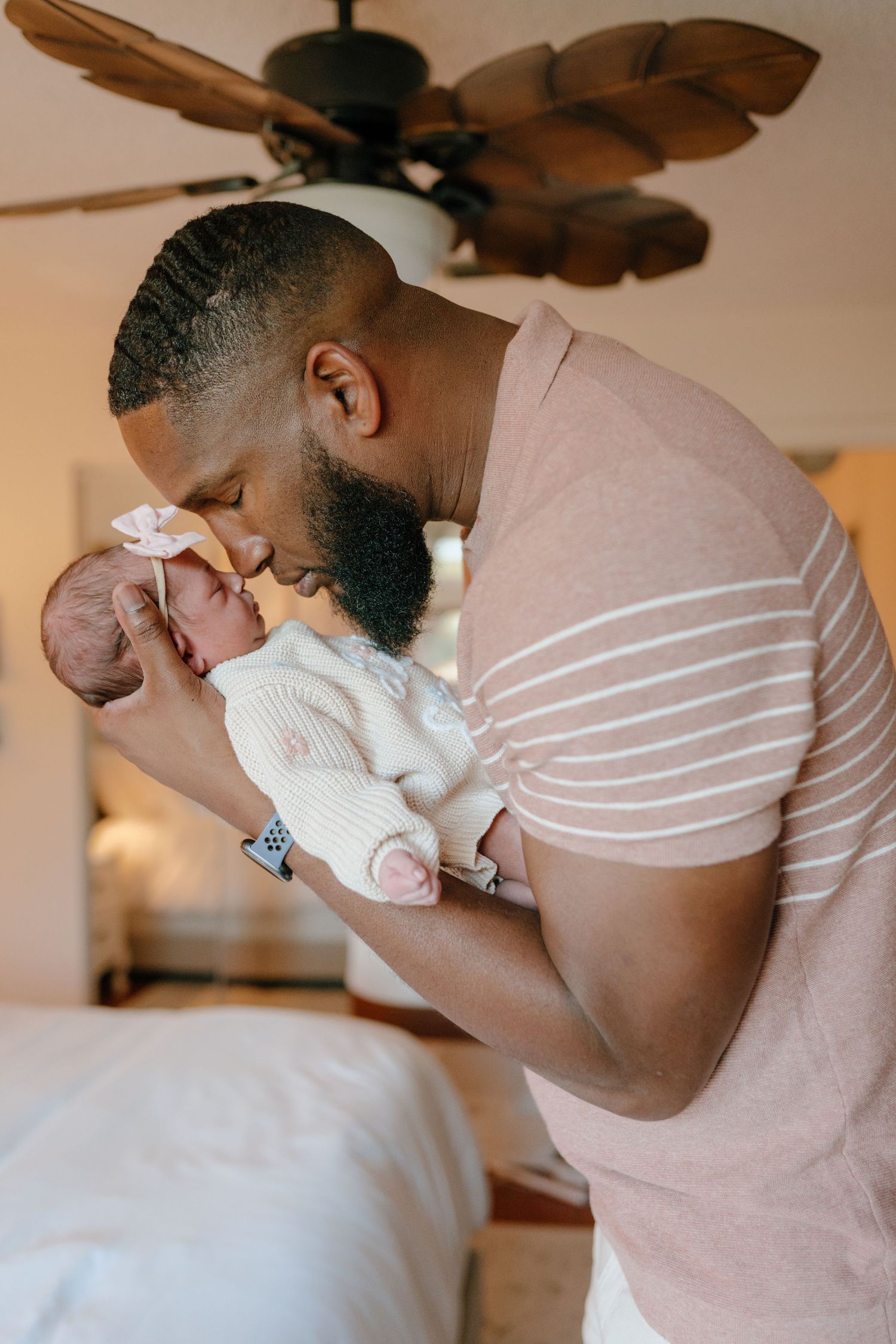 Father gently kissing his newborn baby girl wearing a pink bow headband.