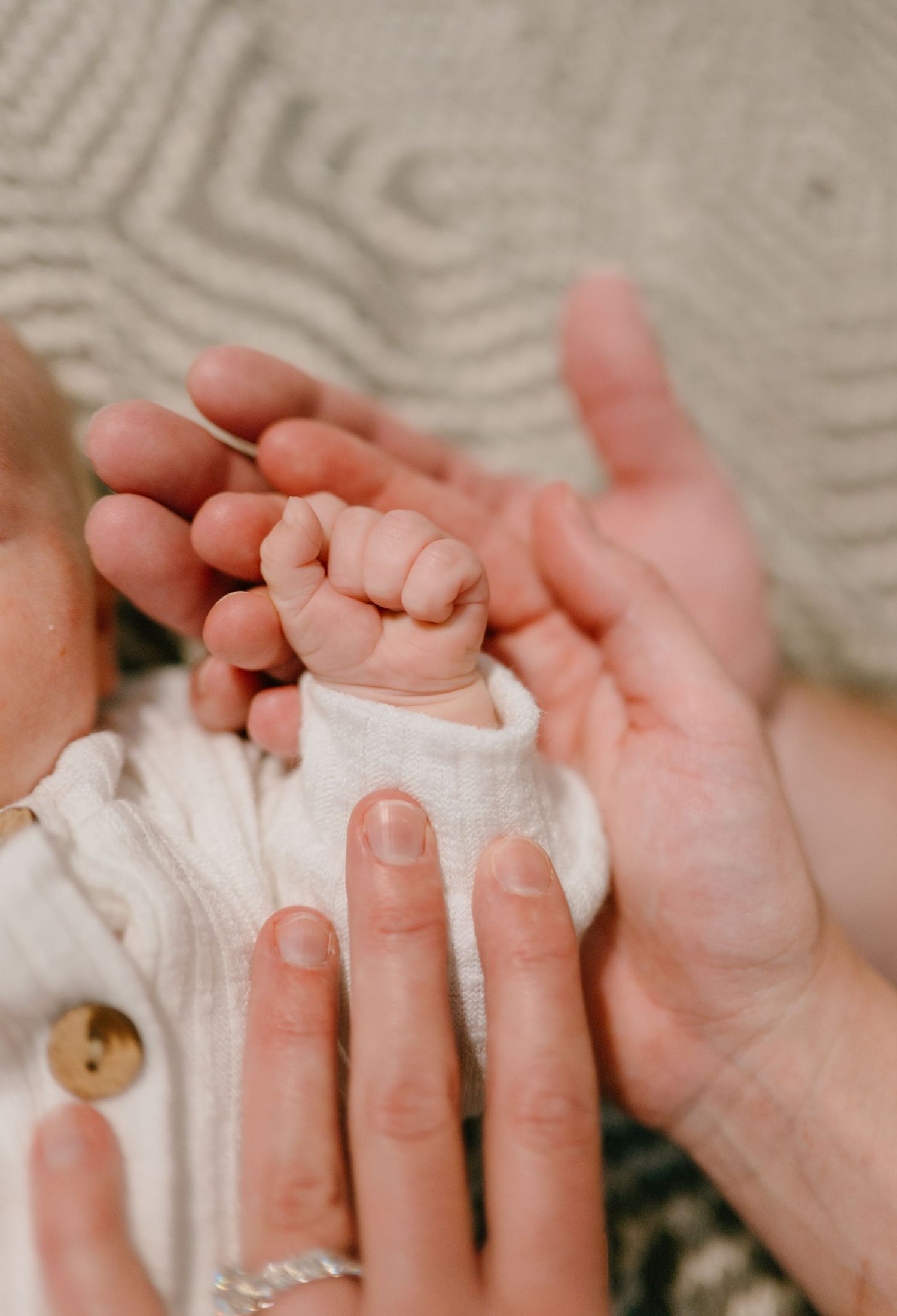 Close-up of a newborn baby's tiny fist resting in a parent's open hands.
