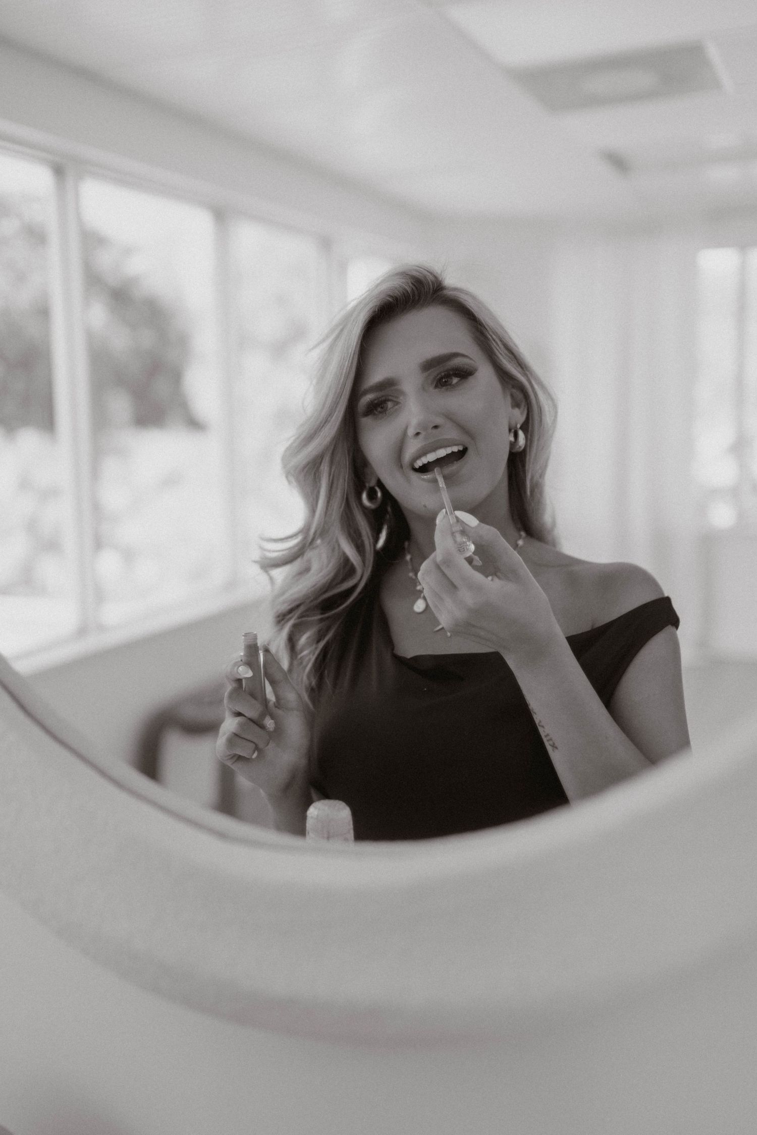 Woman applying lipstick while looking in a round mirror, black and white photo.
