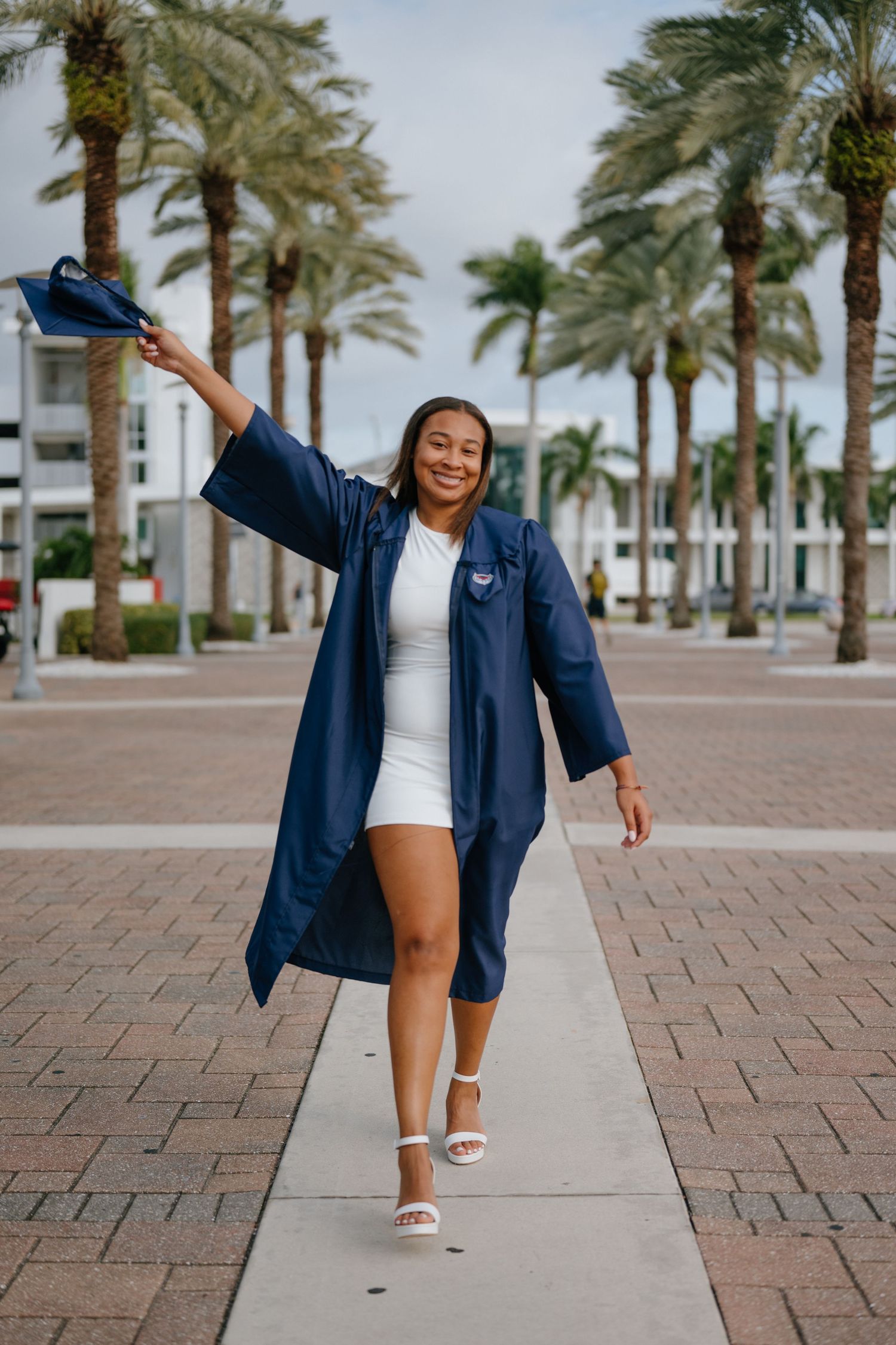 Smiling graduate in navy cap and gown celebrates outdoors among palm trees at FAU campus.