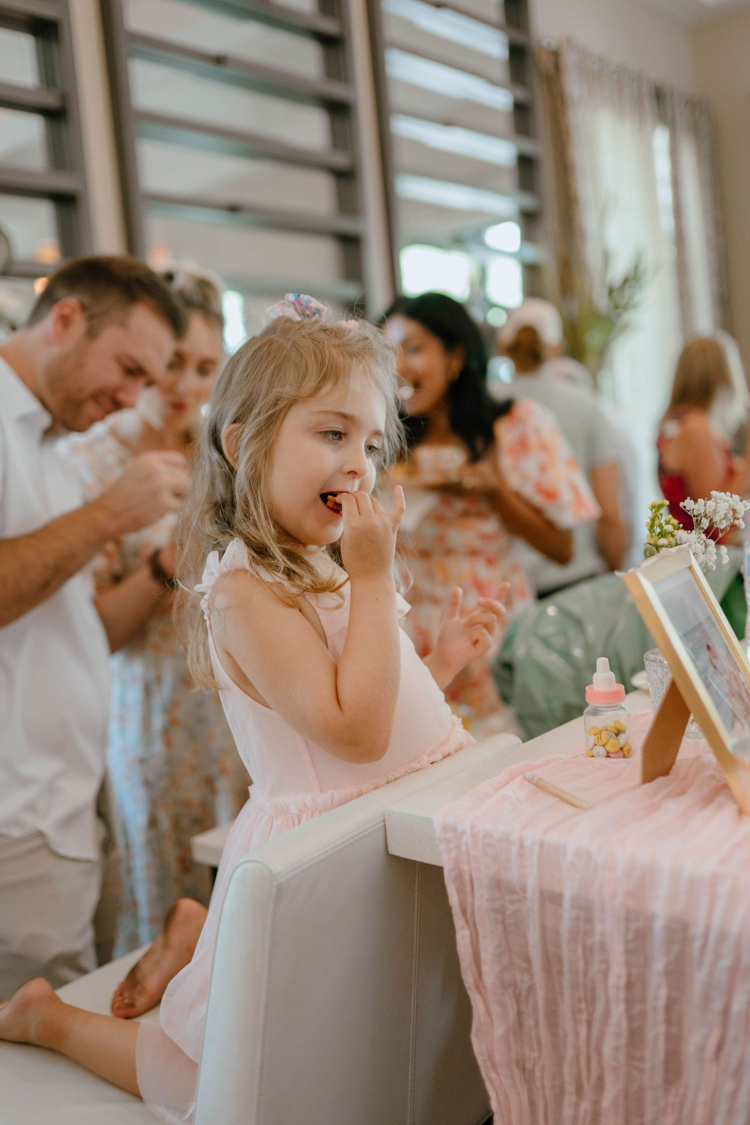 Young girl in pink dress happily eating treats at a baby shower party table.