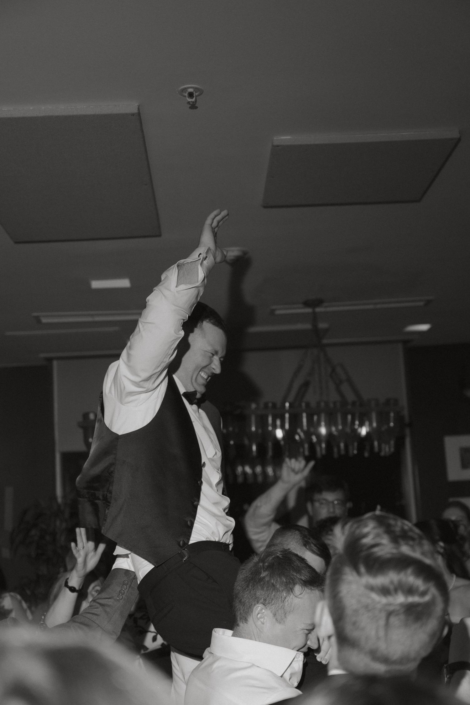 Groom being lifted by guests while celebrating on the dance floor at a wedding reception.