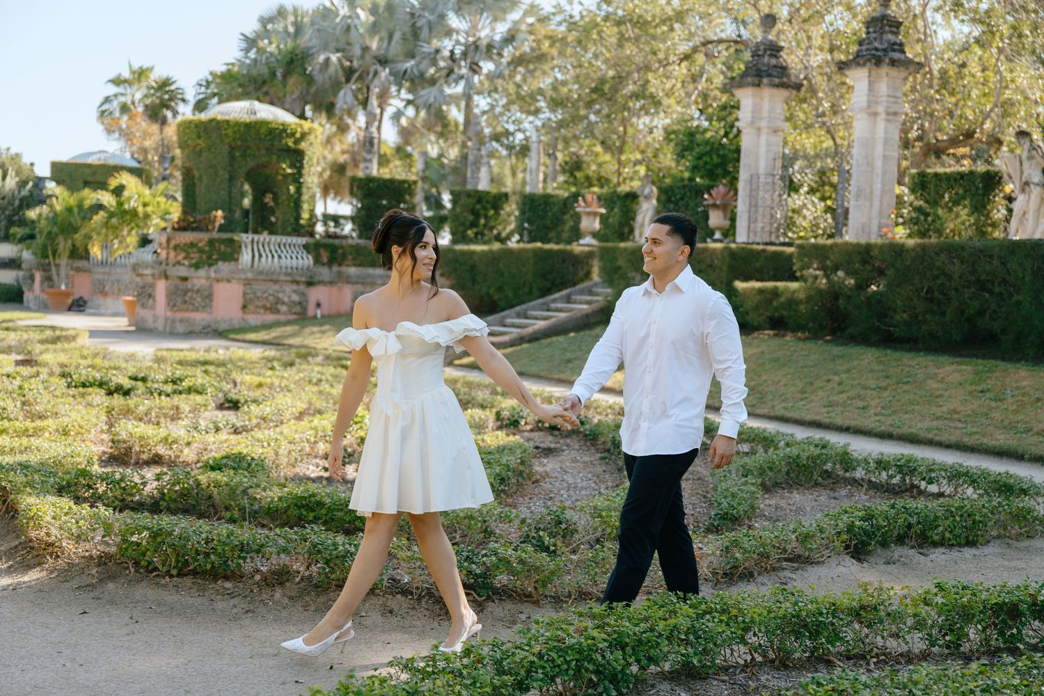 Engaged couple strolling through formal garden maze holding hands at a historic Florida estate.