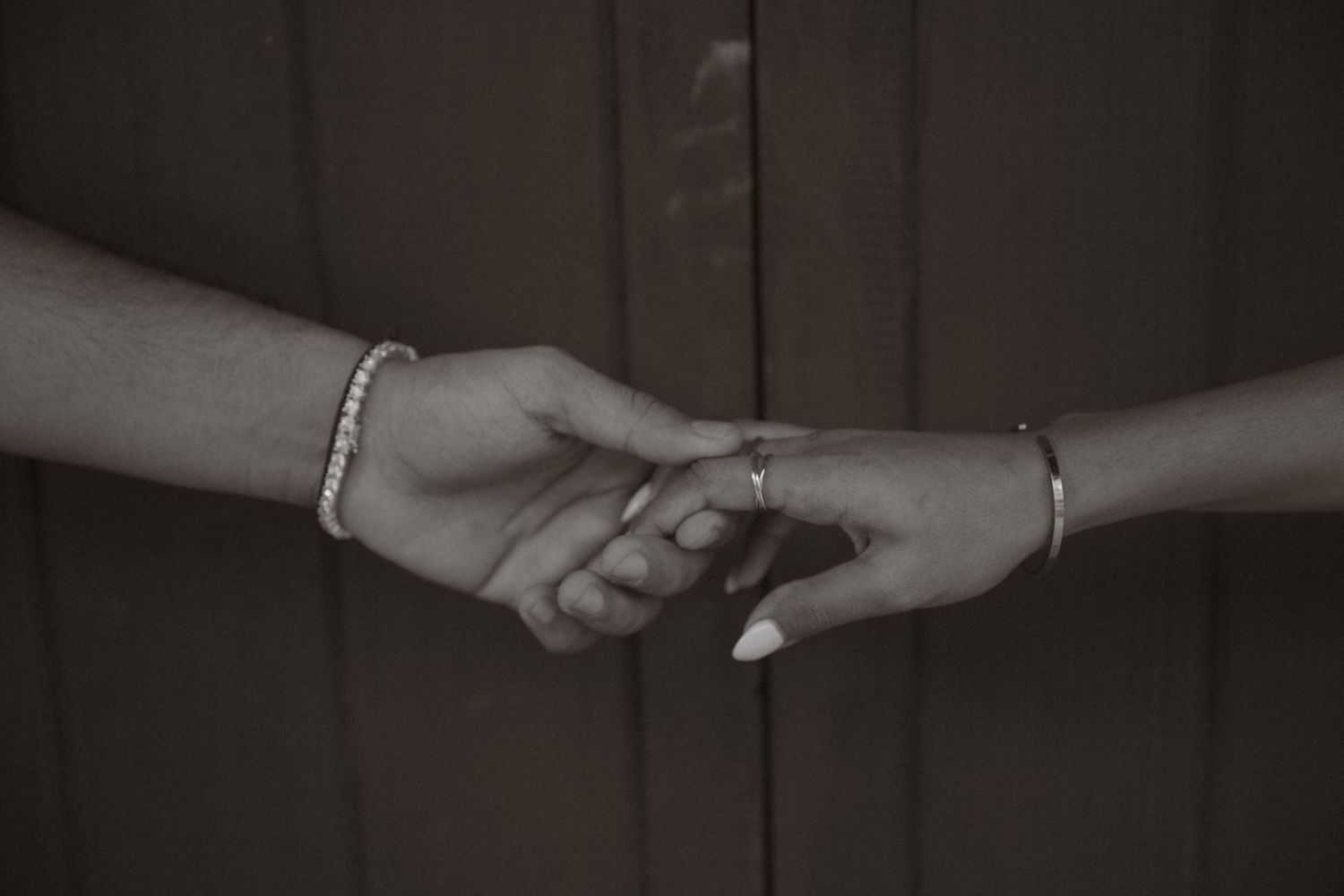 Close-up black and white photo of couple holding hands wearing bracelets and a ring.