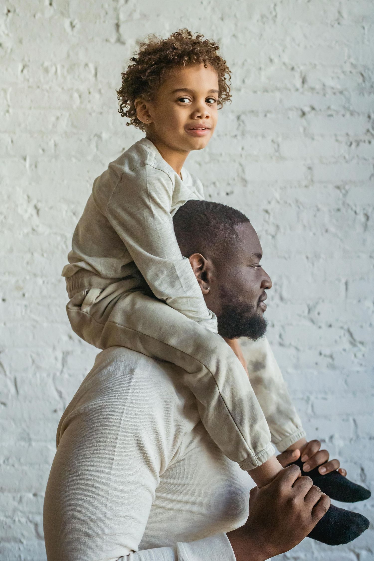 Family casual photoshoot. A heartwarming sequence of a parent giving a piggyback ride to a child against a white brick wall background.