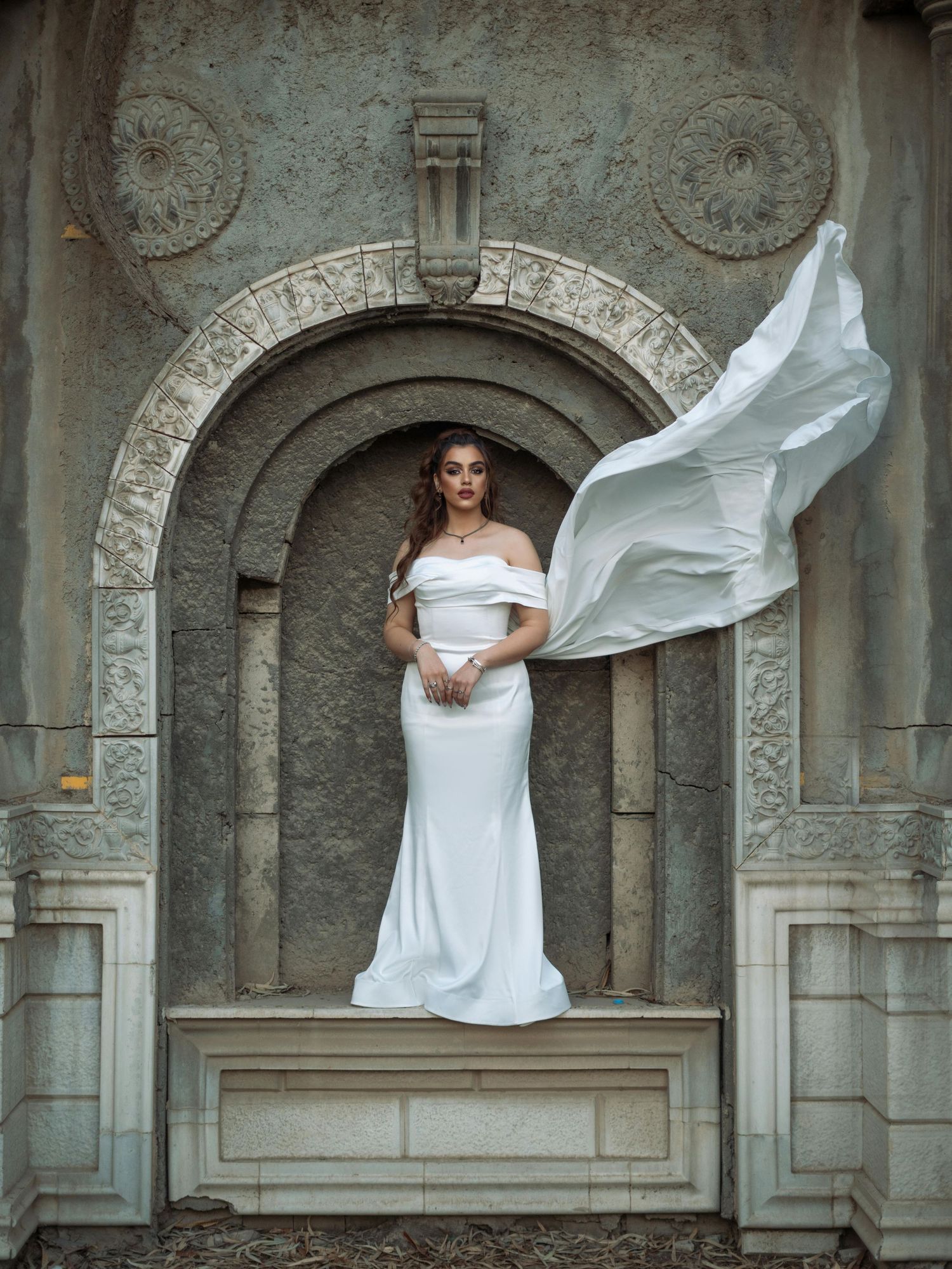 A bride in a flowing white dress poses dramatically against stone archways in an architectural setting. Trusted Flagstaff Photographer.