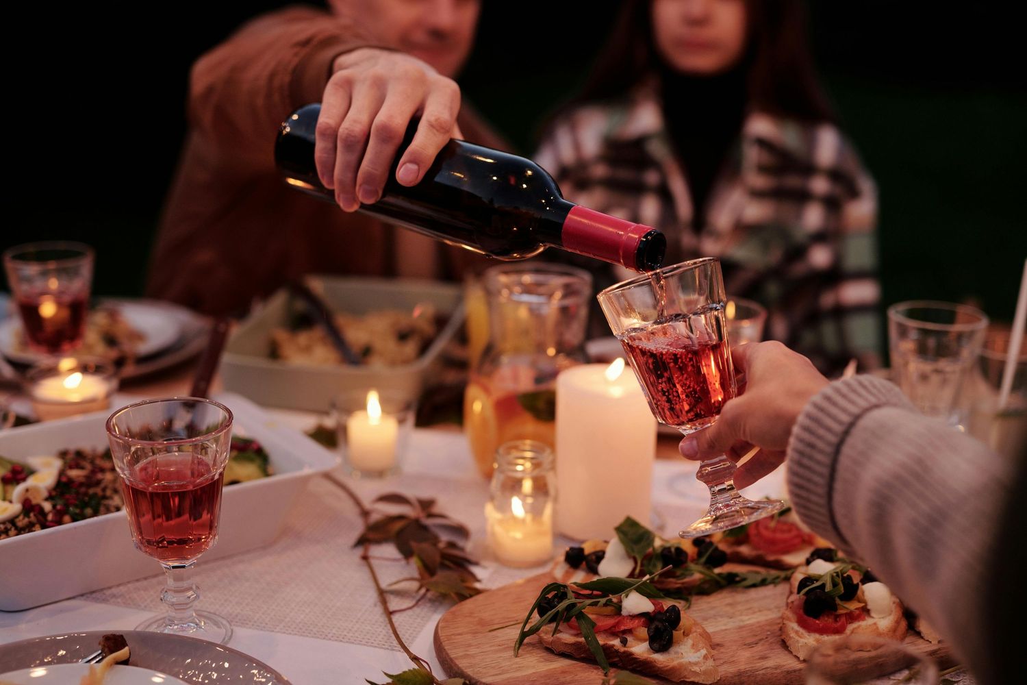 Candlelit table setting with wine glasses and drinks being poured during an evening gathering.