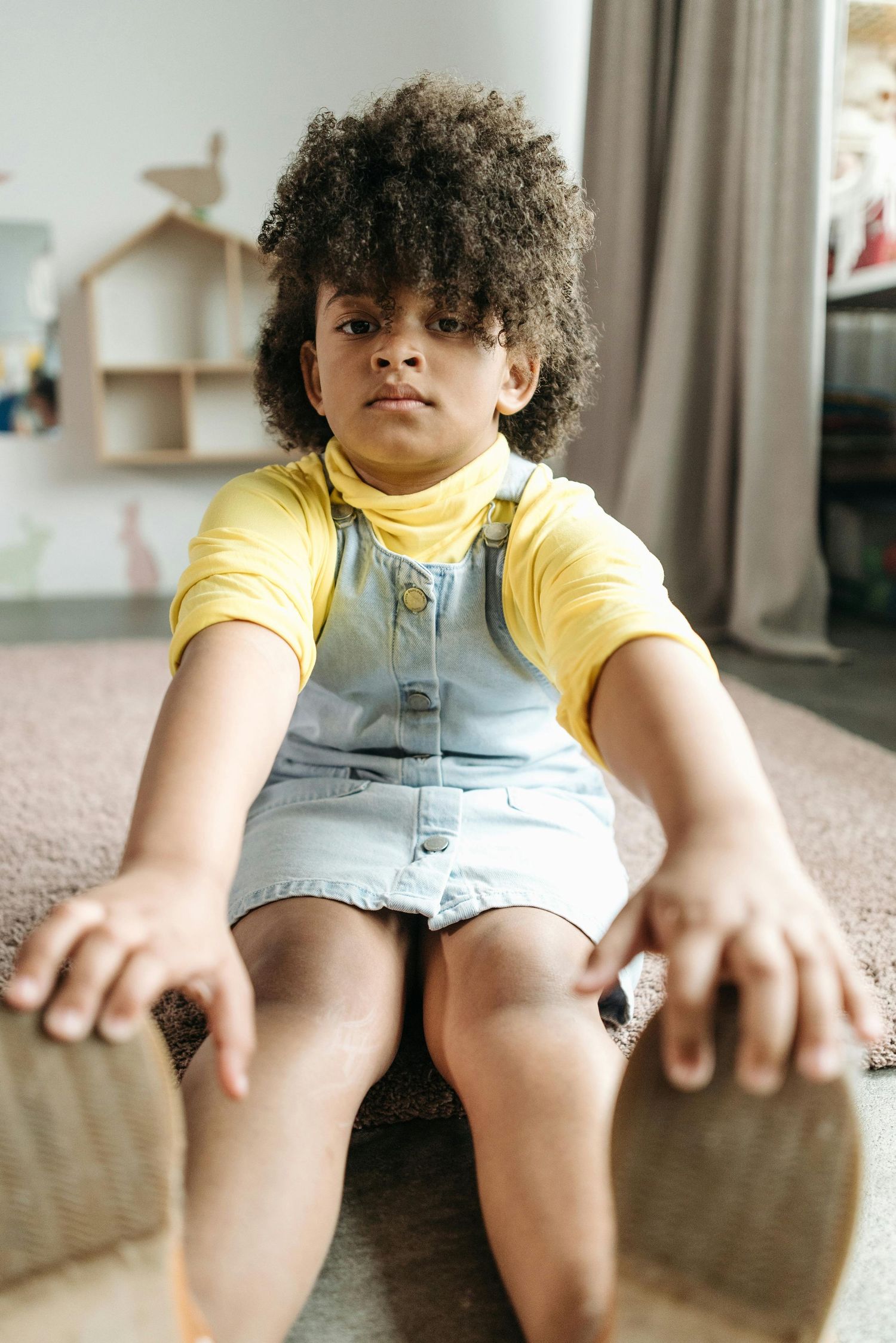Arizona Daycare Photography Child in yellow shirt and denim overalls sitting on carpet.
