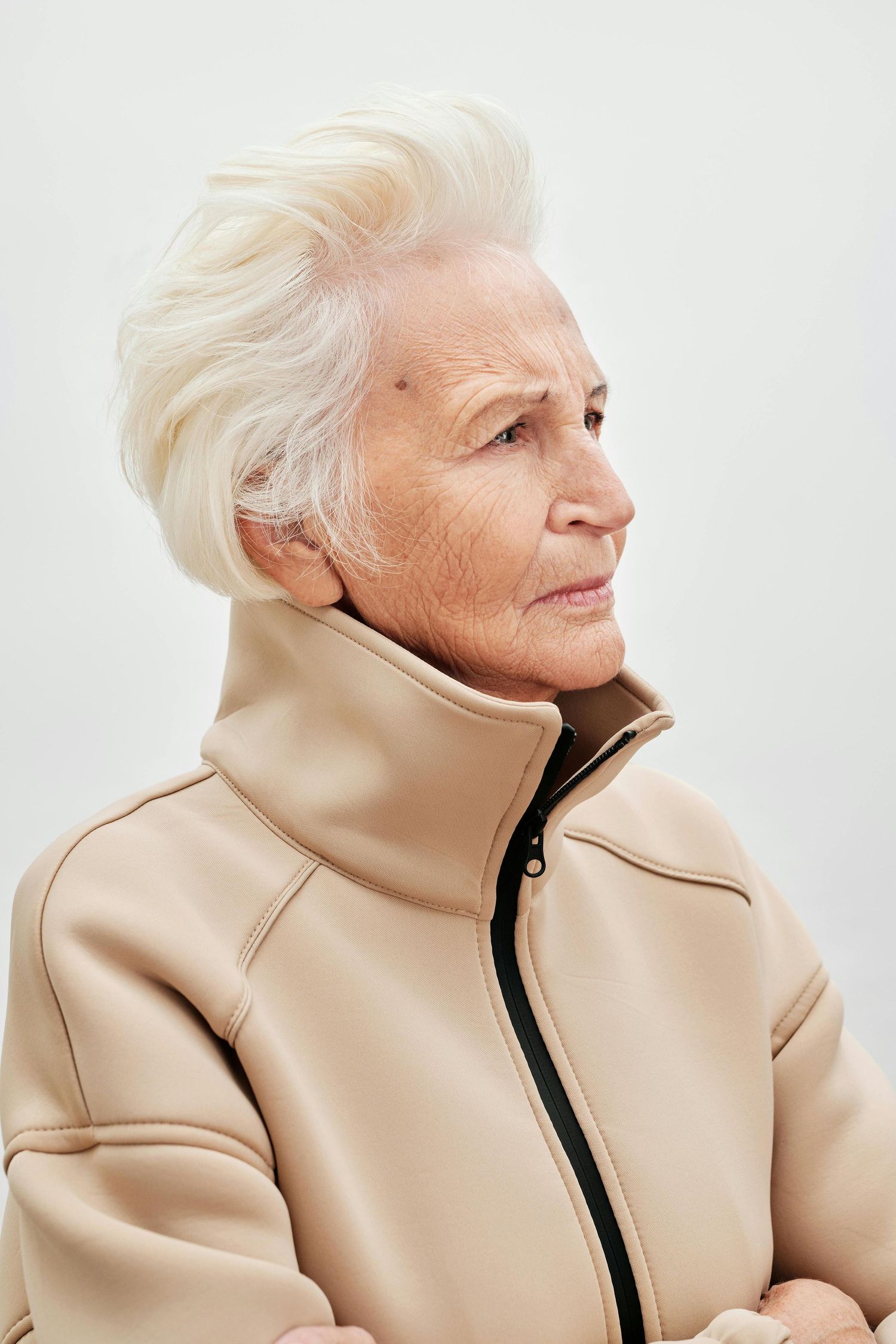 Senior portrait Scottsdale. A person with white hair wearing a beige turtleneck jacket poses against a white background in a profile series.