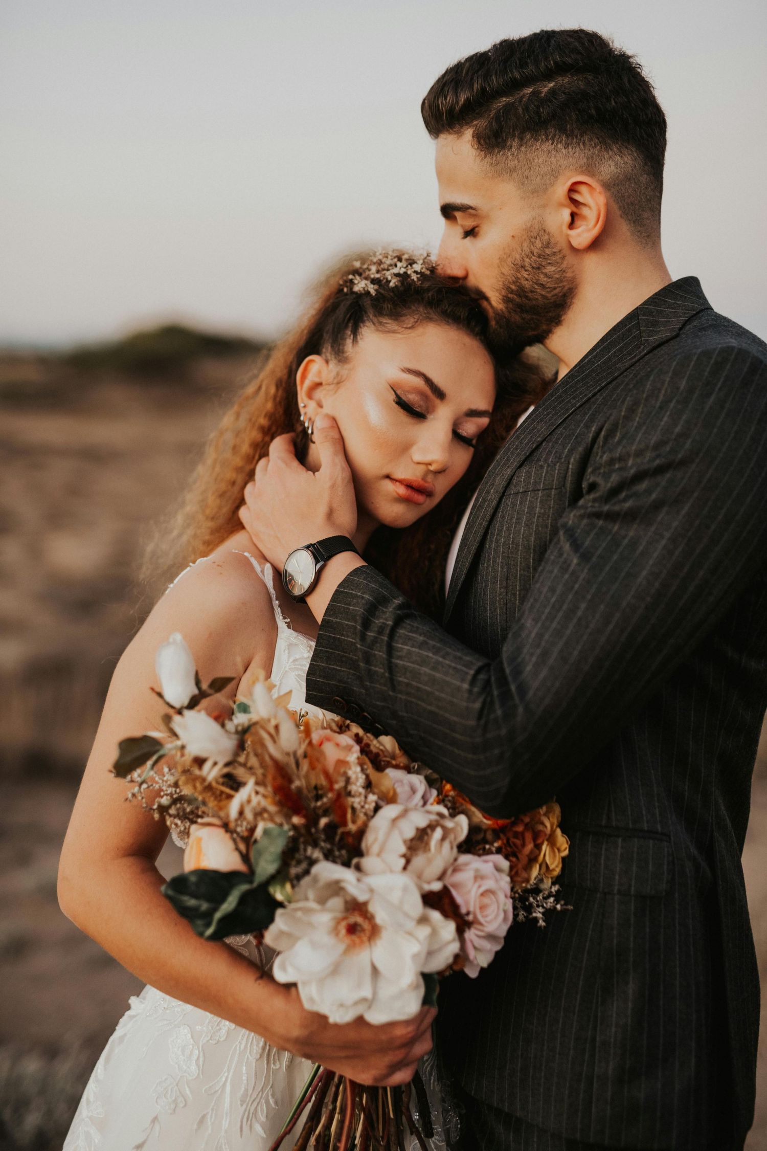 Romantic desert wedding photoshoot with couple embracing while holding a bouquet of blush and white flowers. Trusted Sedona Photographer.