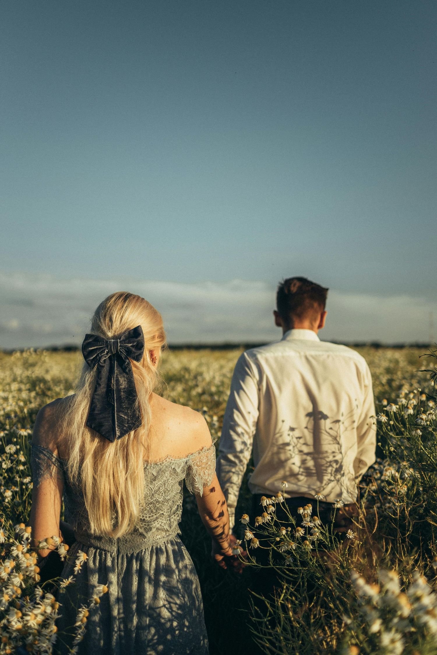 Couple holding hands in wild grass, captured with soft, heartfelt Arizona engagement photography. Fountain Hills.