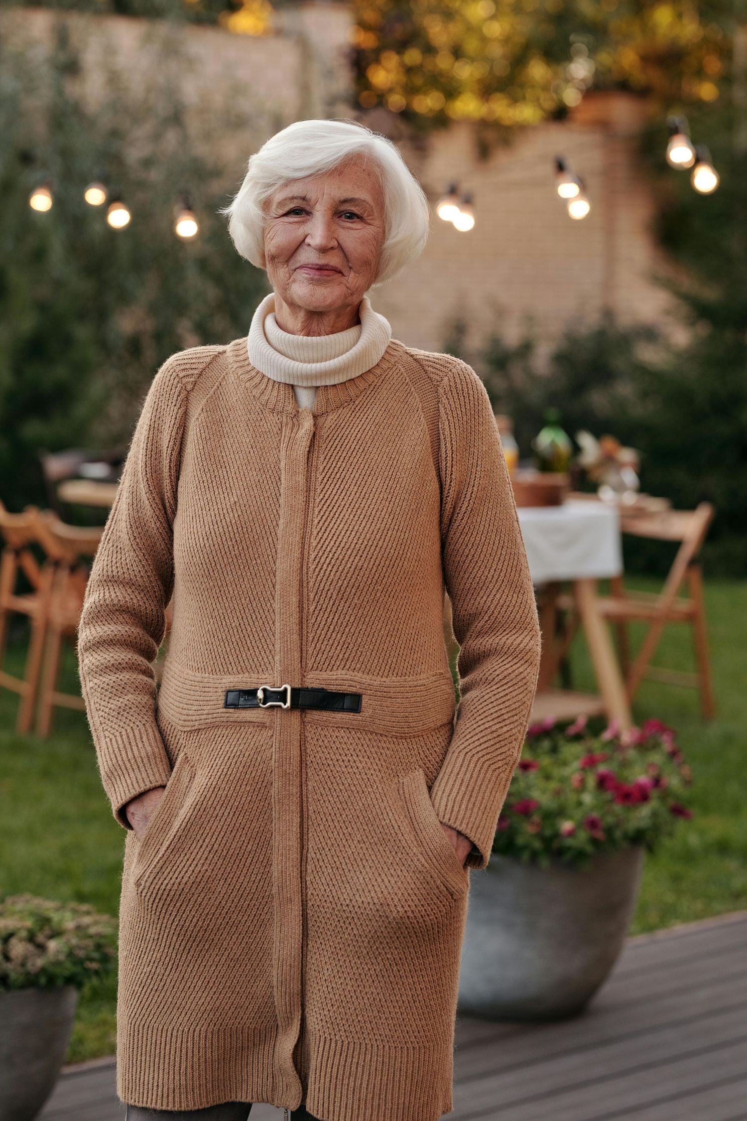 A person wearing cozy beige knit sweater stands in a garden setting with string lights and planters in the background. Desert Ridge Arizona.