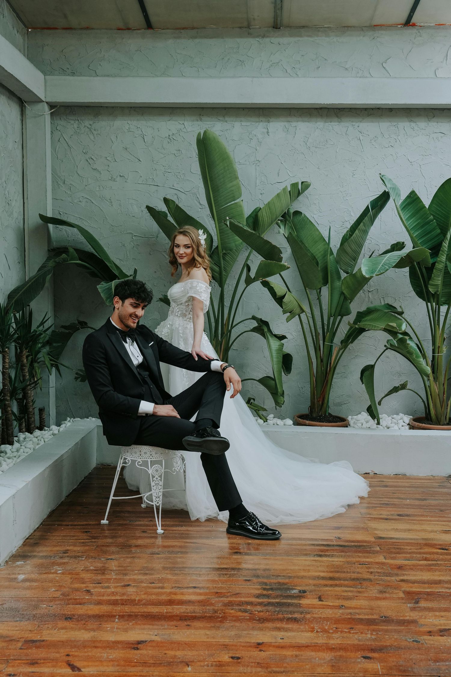 Sequence of wedding couple playfully falling backwards on wooden floor with tropical plants in minimalist white space. Desert Ridge Arizona.