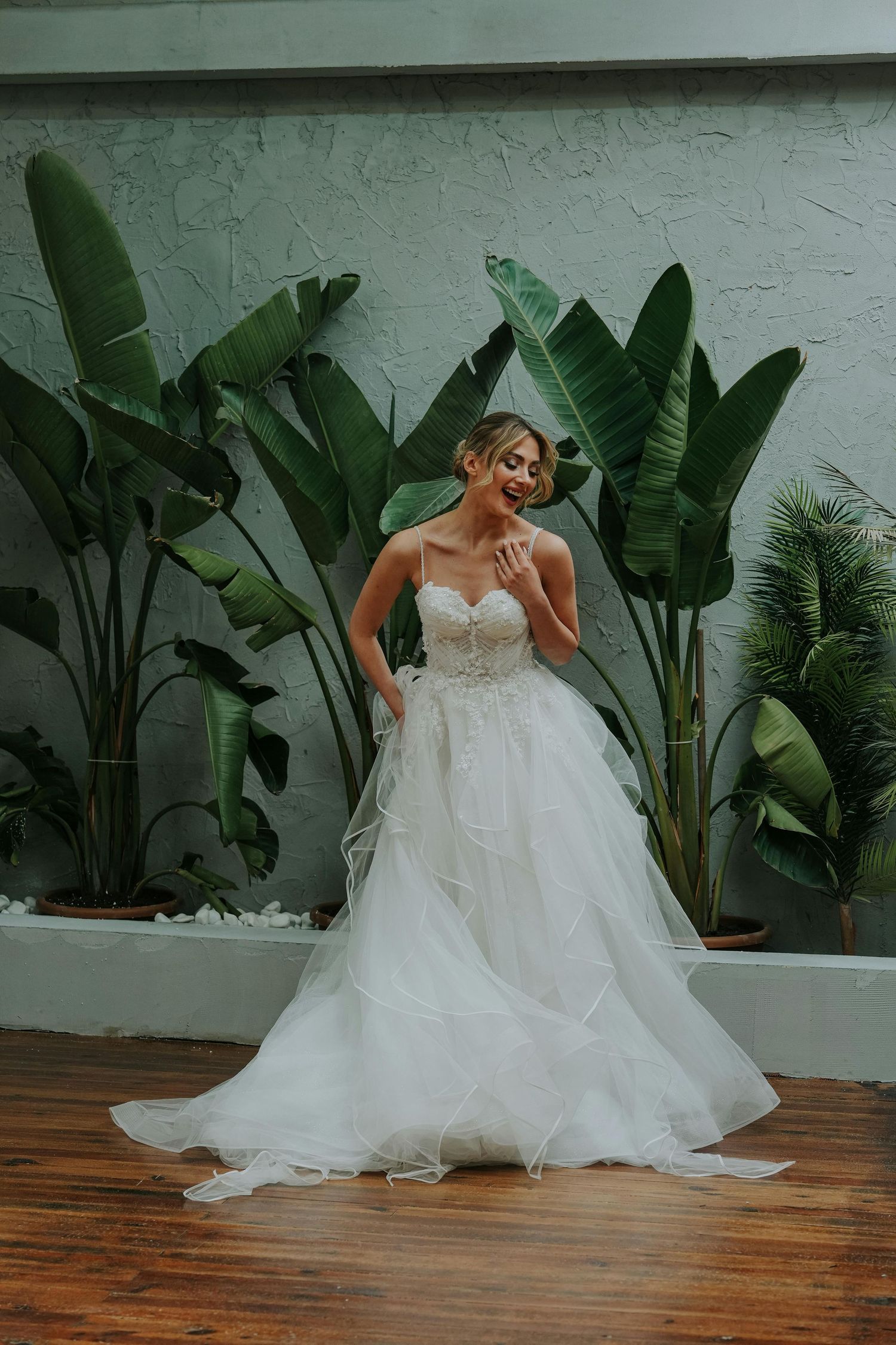 Bride in a flowing white wedding gown poses playfully against a backdrop of tropical plants and wooden floors. Leading Arizona Photographer