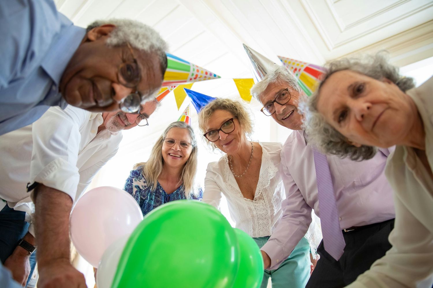 Festive party scene with people playing with green and pink balloons under yellow banner decorations.