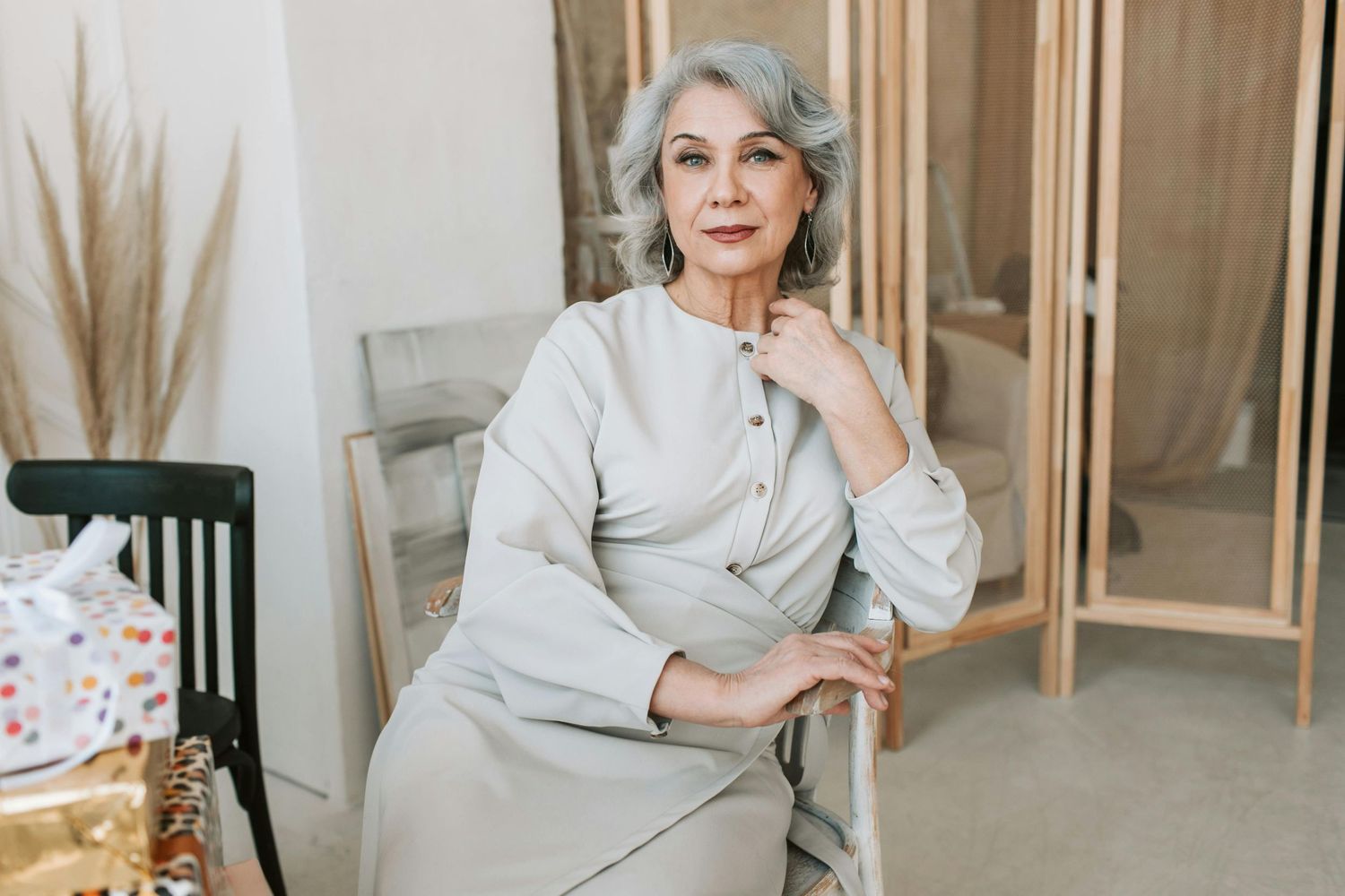 Elegant woman with silver hair wearing a beige sweater sits confidently in a modern interior setting.