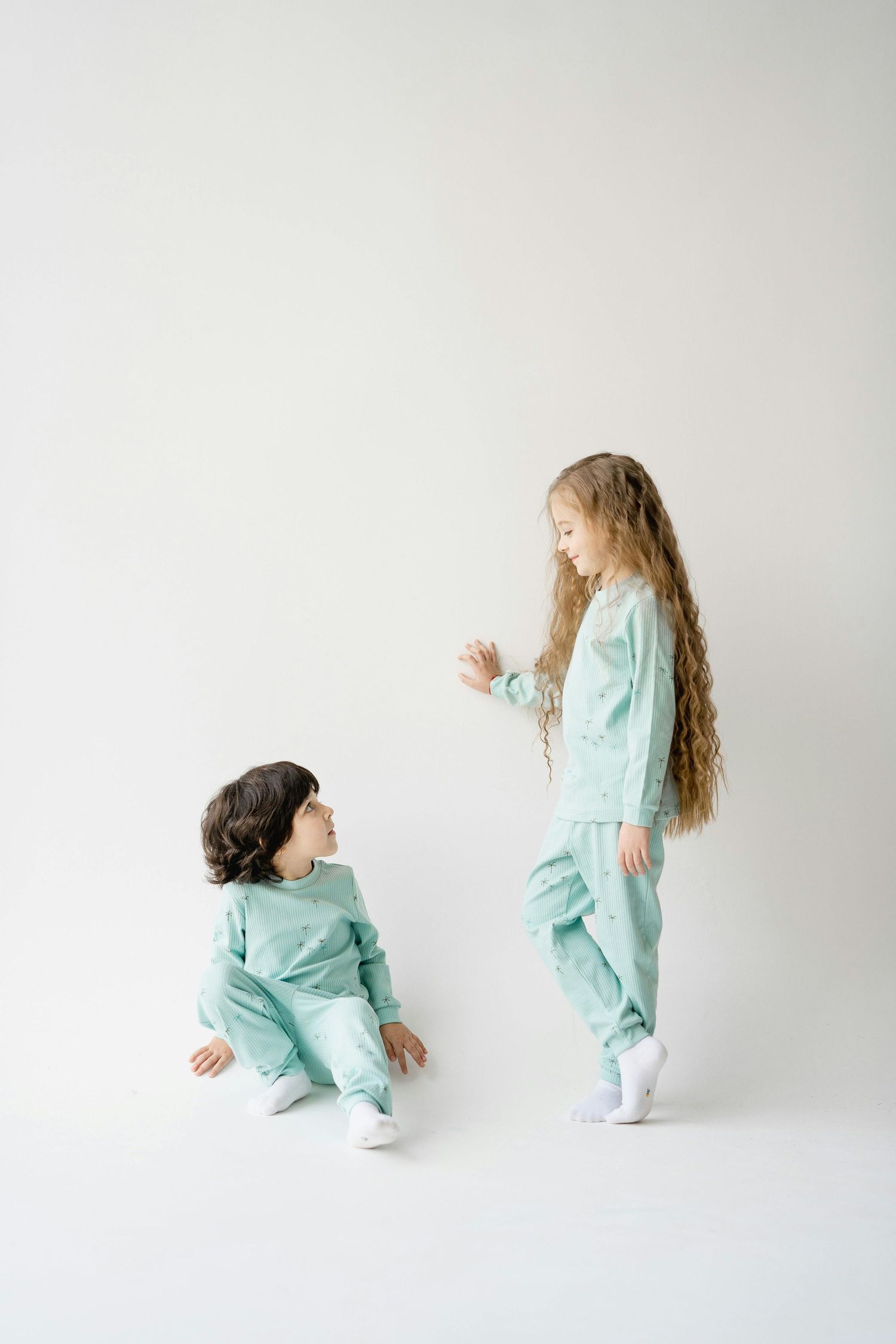 Two children in matching mint green outfits stand together against a white backdrop.