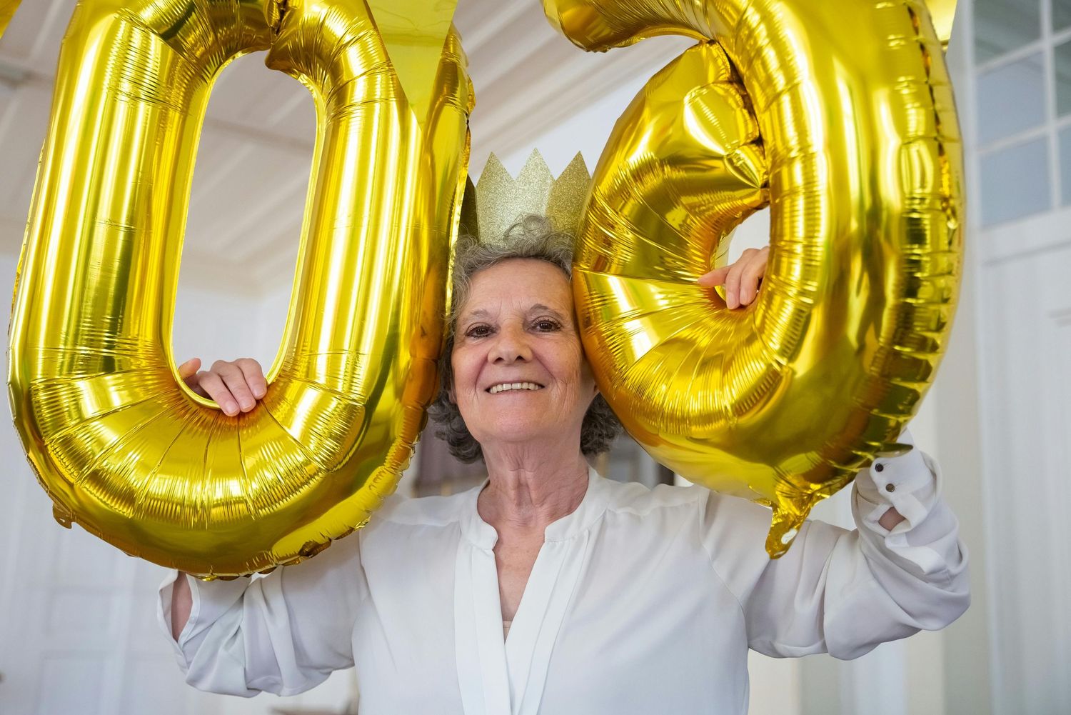 Gold letter balloons spelling out text are held up against a white wall in a celebratory display.
