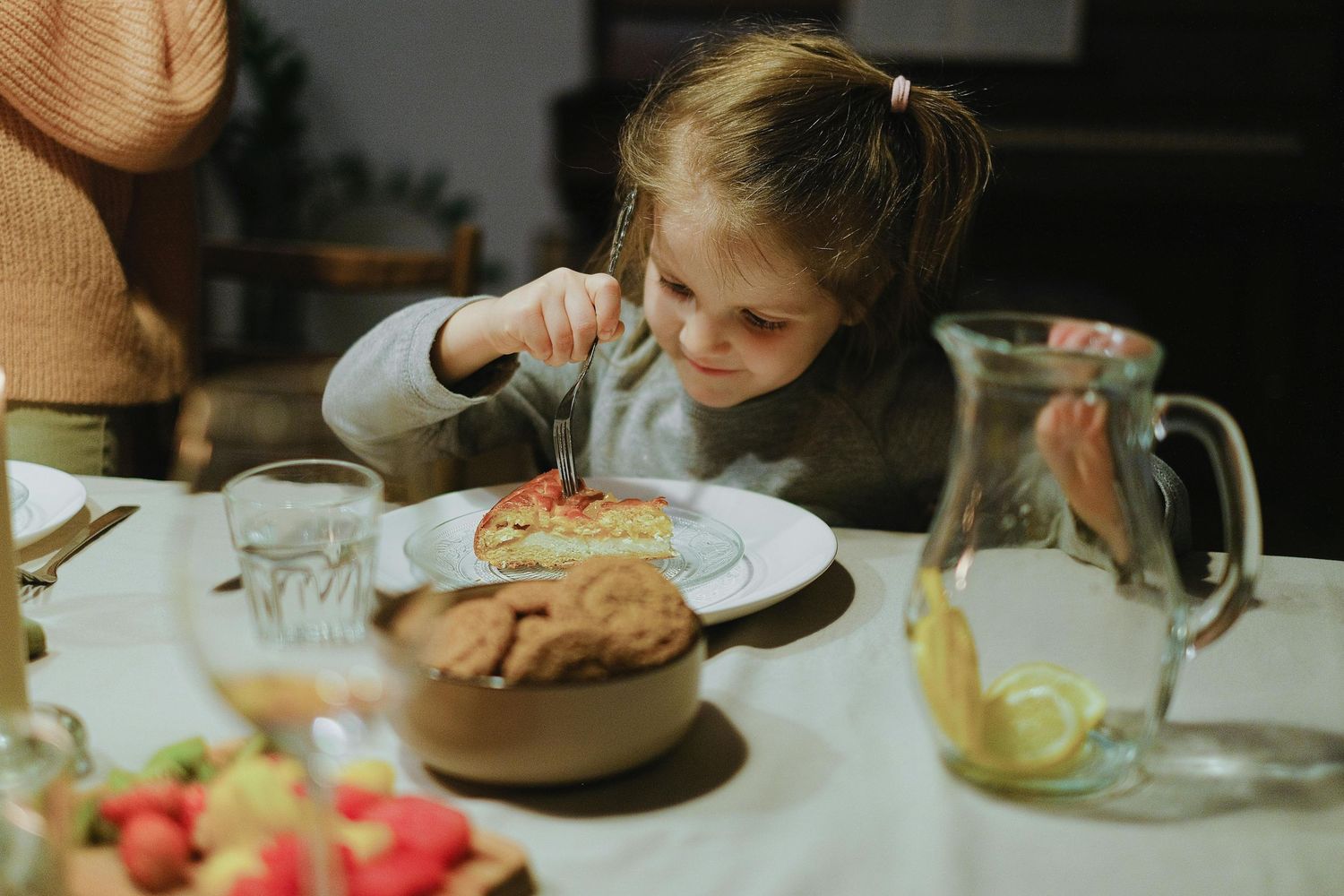 People gathered around a dining table with plates and food in warm indoor lighting.