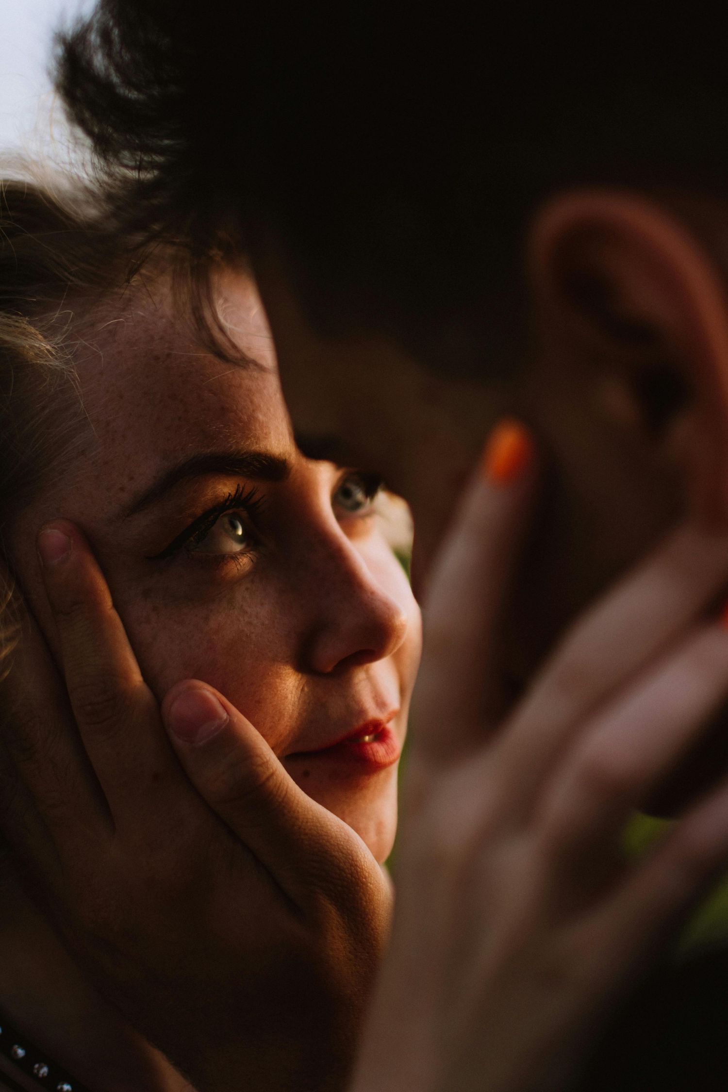 Close-up portrait in dramatic lighting shows a face with red lipstick and contemplative gaze in shadow. Strawberry Arizona