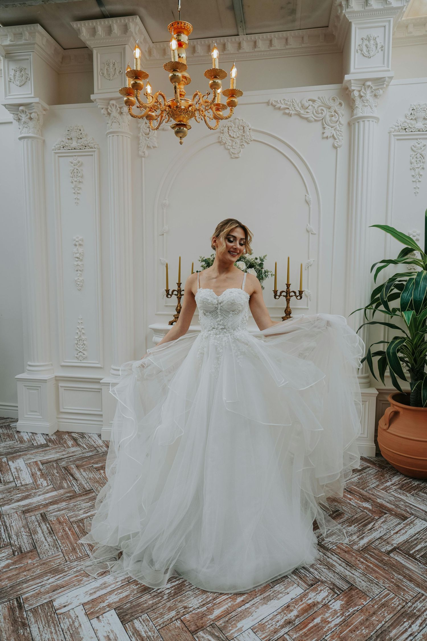 A bride in an elegant ballgown twirls gracefully in an ornate white room with chandelier and herringbone floors. Top Photographer Scottsdale