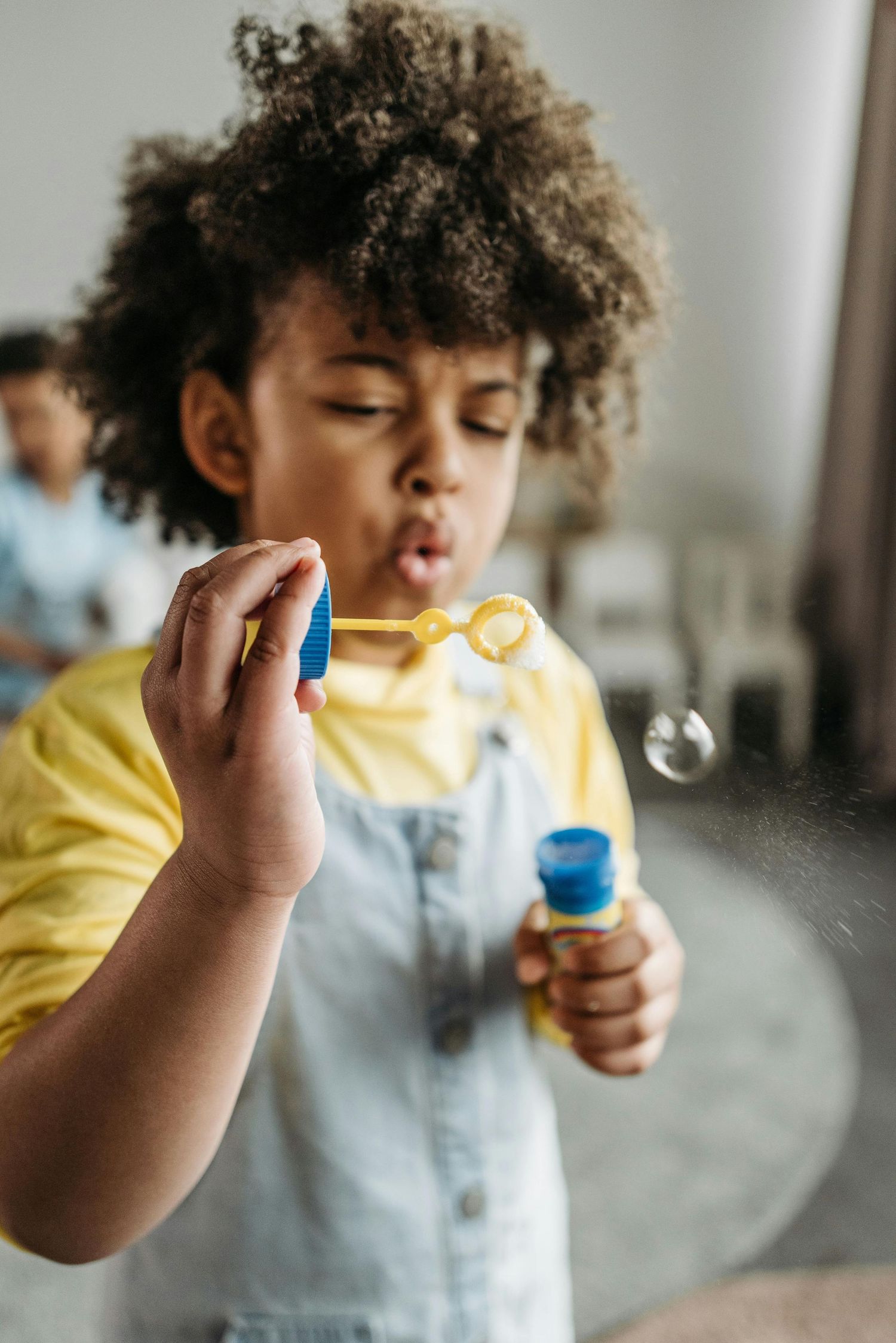 Arizona Daycare Photography Child in yellow shirt blowing bubbles in indoor setting.