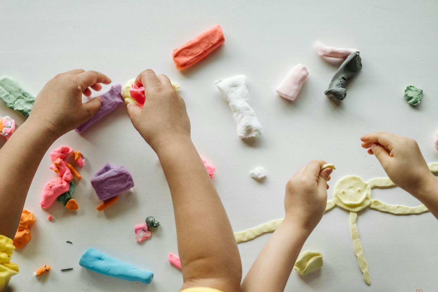 Arizona Daycare Photography Hands playing with colorful modeling clay and craft materials on a white surface.