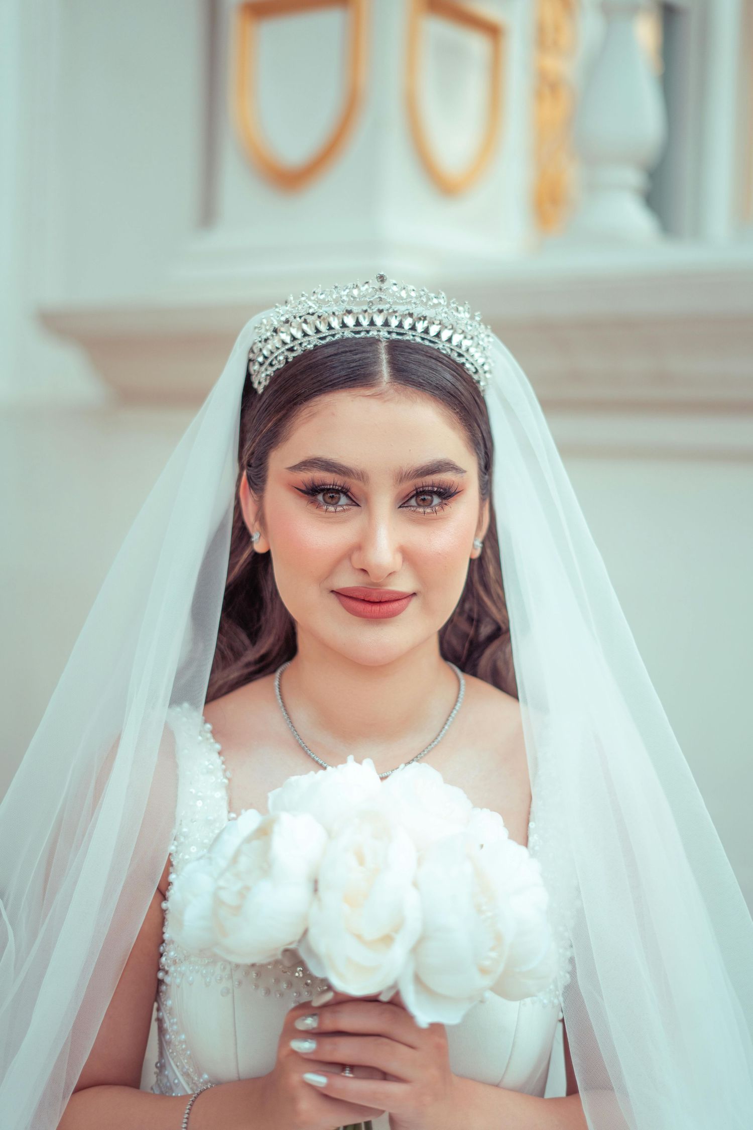 A bride wearing a white veil and tiara poses with white roses in a series of wedding portraits. Award Winning Photographer Tempe